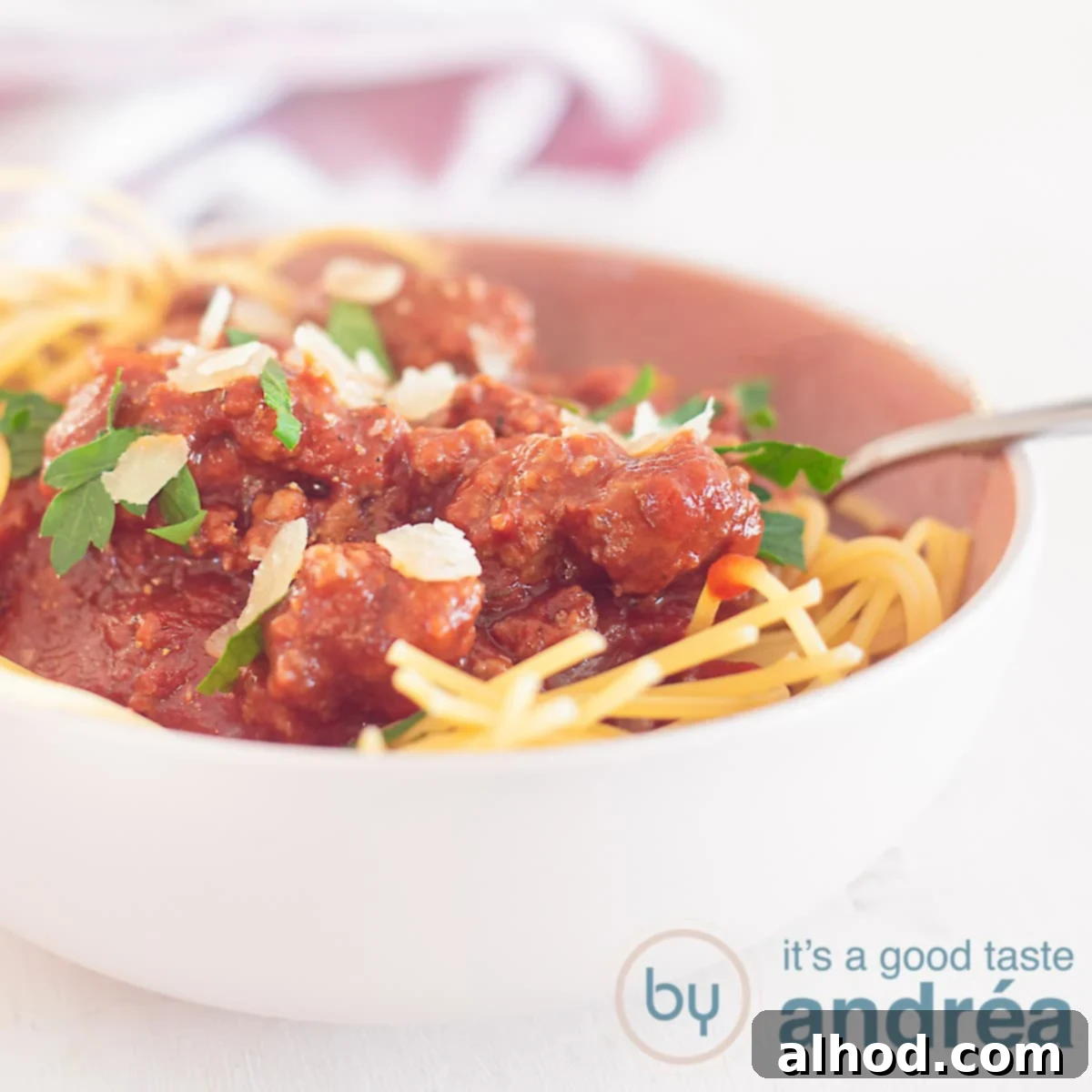 Ragù alla Bolognese 6 A square photo with a pink bowl filled with spaghetti and bolognaise sauce. A white background with a pink tea towel