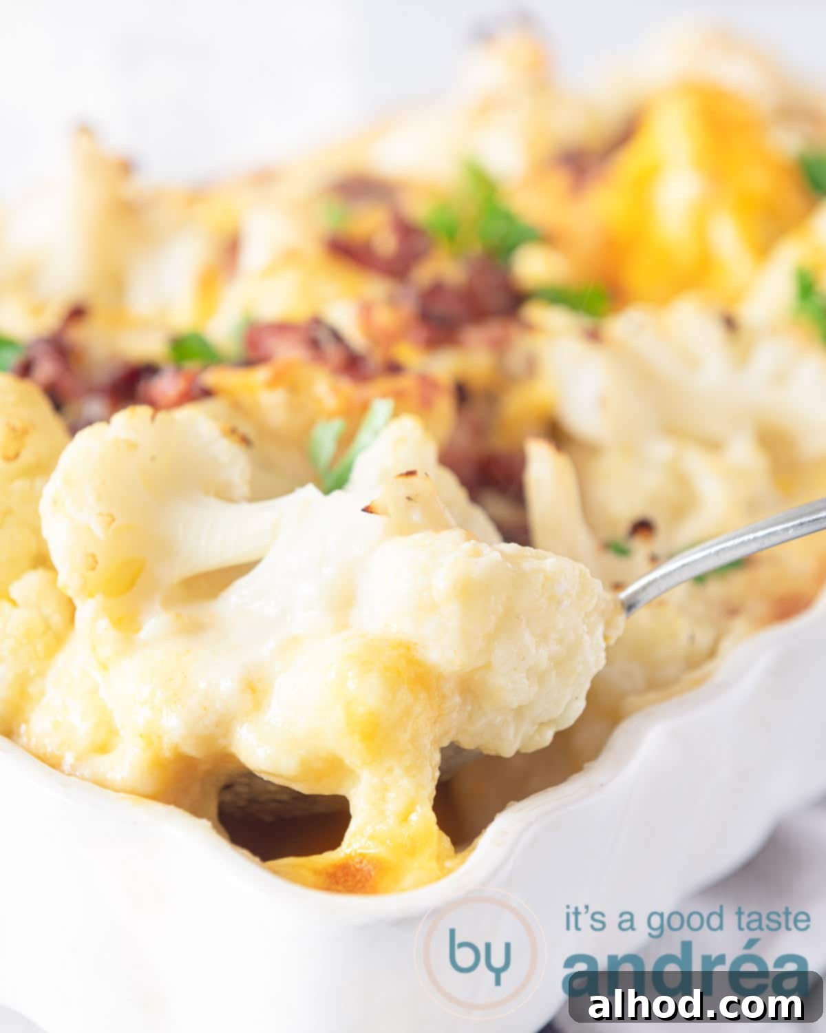 Savory Cheesy Sausage and Cauliflower Bake 5 A serving spoon scooping a portion of the bubbling, golden Cheesy Sausage and Cauliflower Casserole from a white baking dish, showcasing the creamy texture and melted cheese.