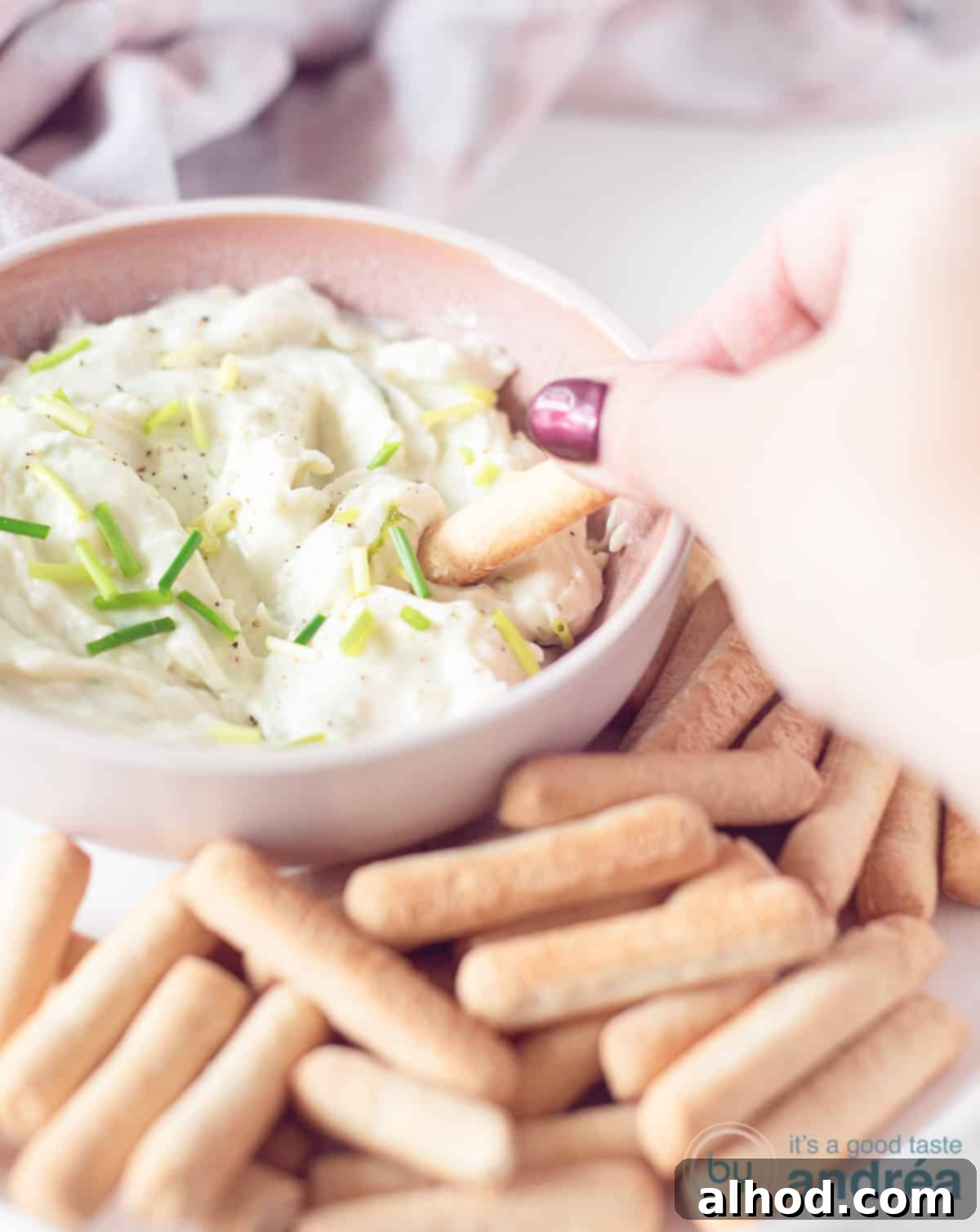 Creamy Gorgonzola Delight 3 A height photo with a pink container with blue cheese dip. A breadstick dips in it. More breadsticks around it.