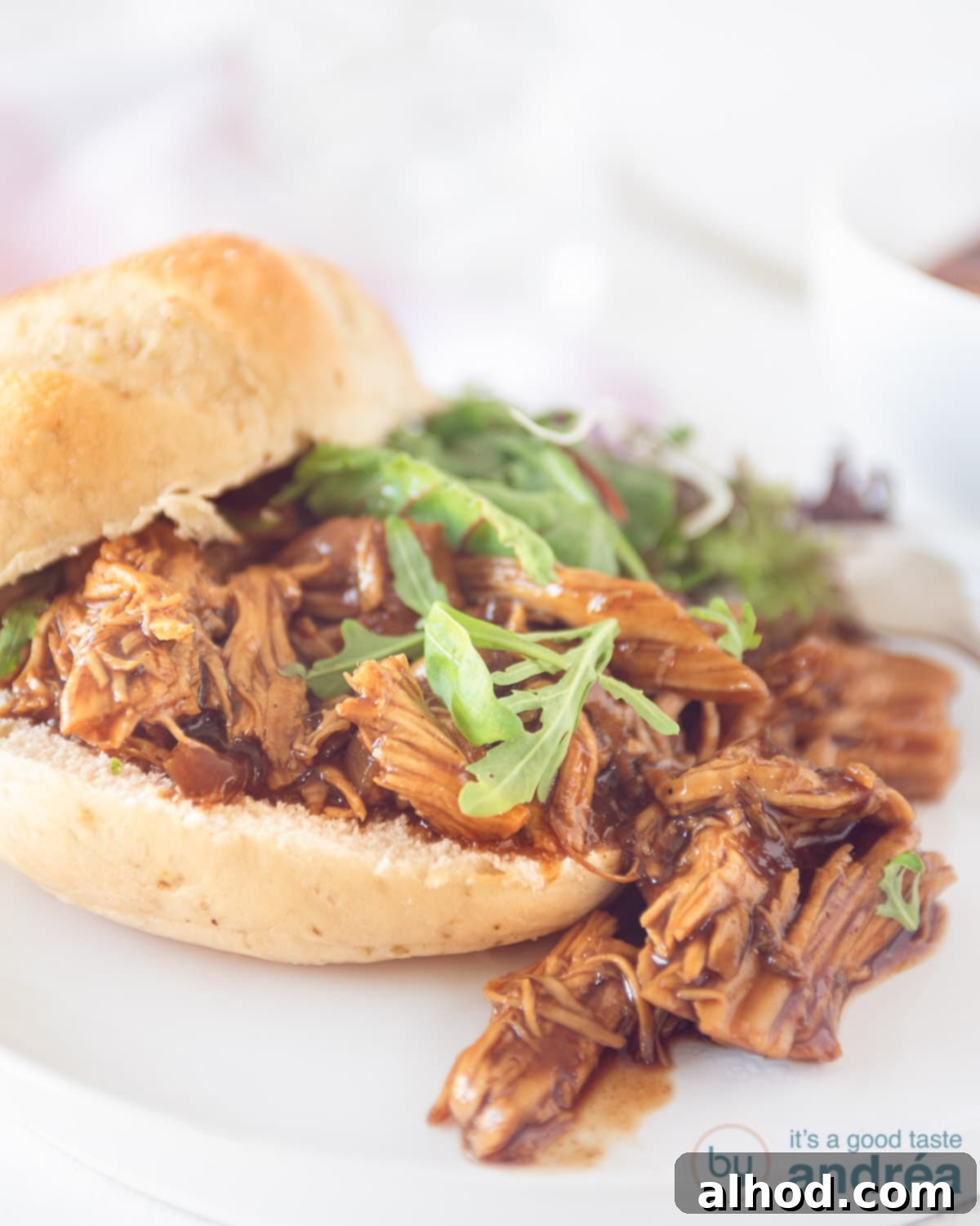 Effortless Slow Cooker BBQ Pulled Chicken 3 A height photo with a pulled chicken sandwich with salad on top. A white background.