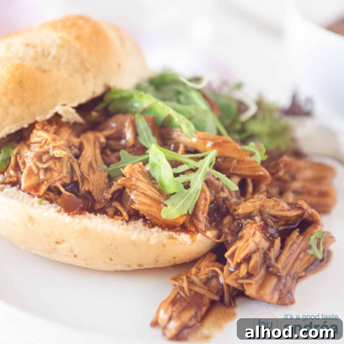Effortless Slow Cooker BBQ Pulled Chicken 4 A square photo with a sandwich with pulled chicken and a salad. on a white background.