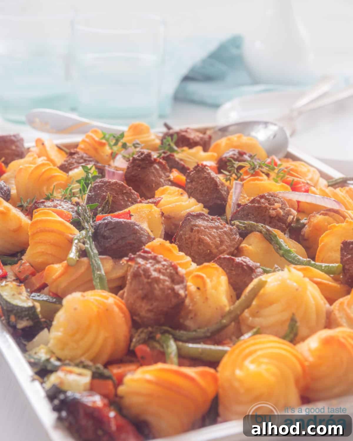 Easy Sheet Pan Burgers with Fluffy Duchess Potatoes 3 A height photo with a gray baking tray with pommes duchesse, roasted vegetables and pieces of hamburger. In the background a tea towel and glasses.