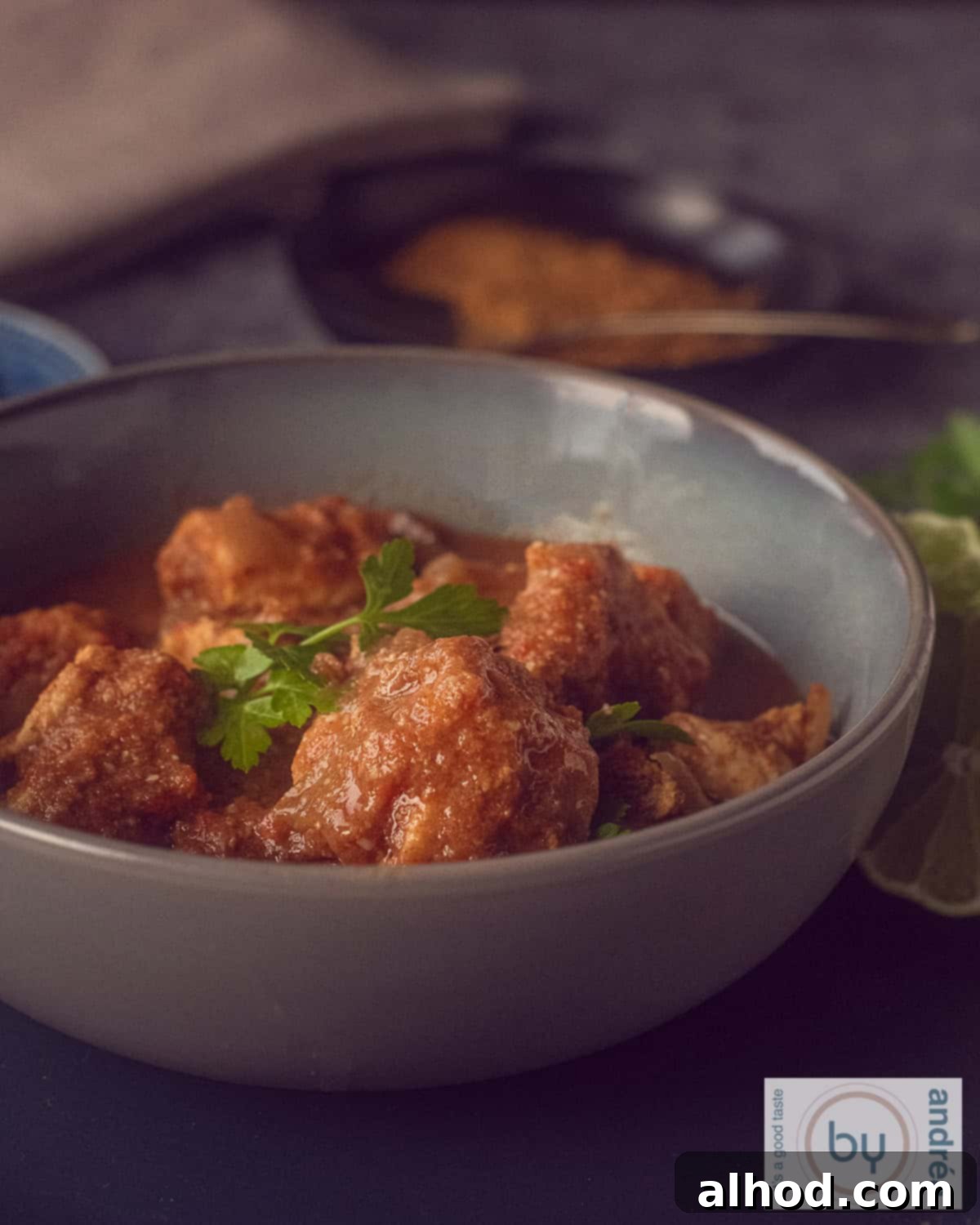 Crockpot Creamy Coconut Chicken Curry 3 A high-angle photograph showing a pink bowl generously filled with spicy chicken curry and its delectable sauce. The background is white, with a pink and white tea towel subtly accenting the scene.
