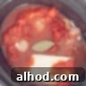 A slow cooker with chicken, herbs, coconut and diced tomatoes. A bay leaf floats in the center.