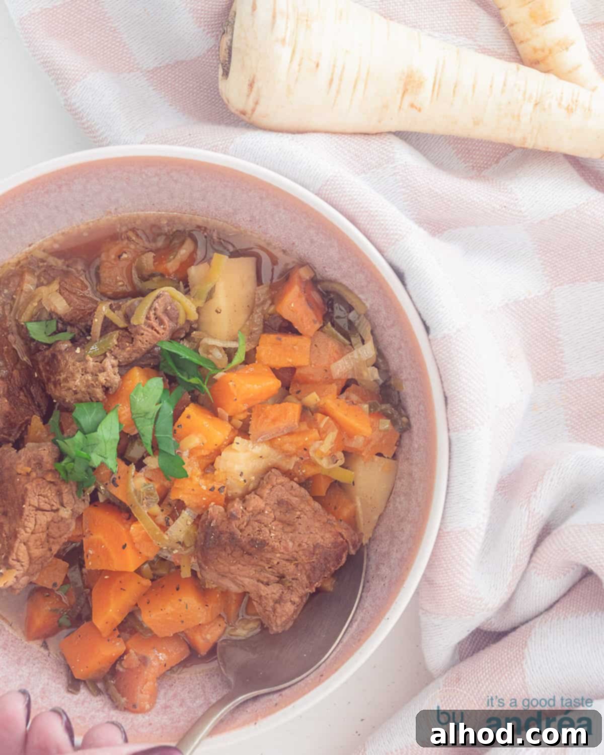 Slow-Simmered Beef and Root Vegetable Stew 2 A photo from above with a pink bowl with stewed beef with carrot, sweet potato and parsnip in a beer broth sauce at the bottom left.