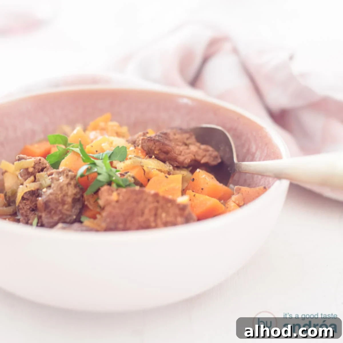 Slow-Simmered Beef and Root Vegetable Stew 4 A square photo with a pink bowl filled with beef stew with winter vegetables in a beer broth sauce on a white background.