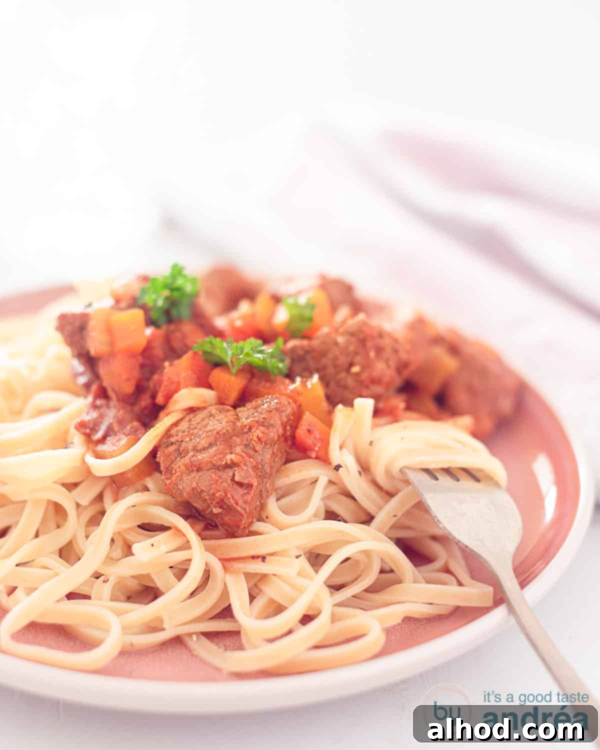 Slow-Simmered Italian Beef Spezzatino 3 A height photo with Spezzatino de Manzo on a bed of tagliatelle. Made in the slow cooker. A white background.