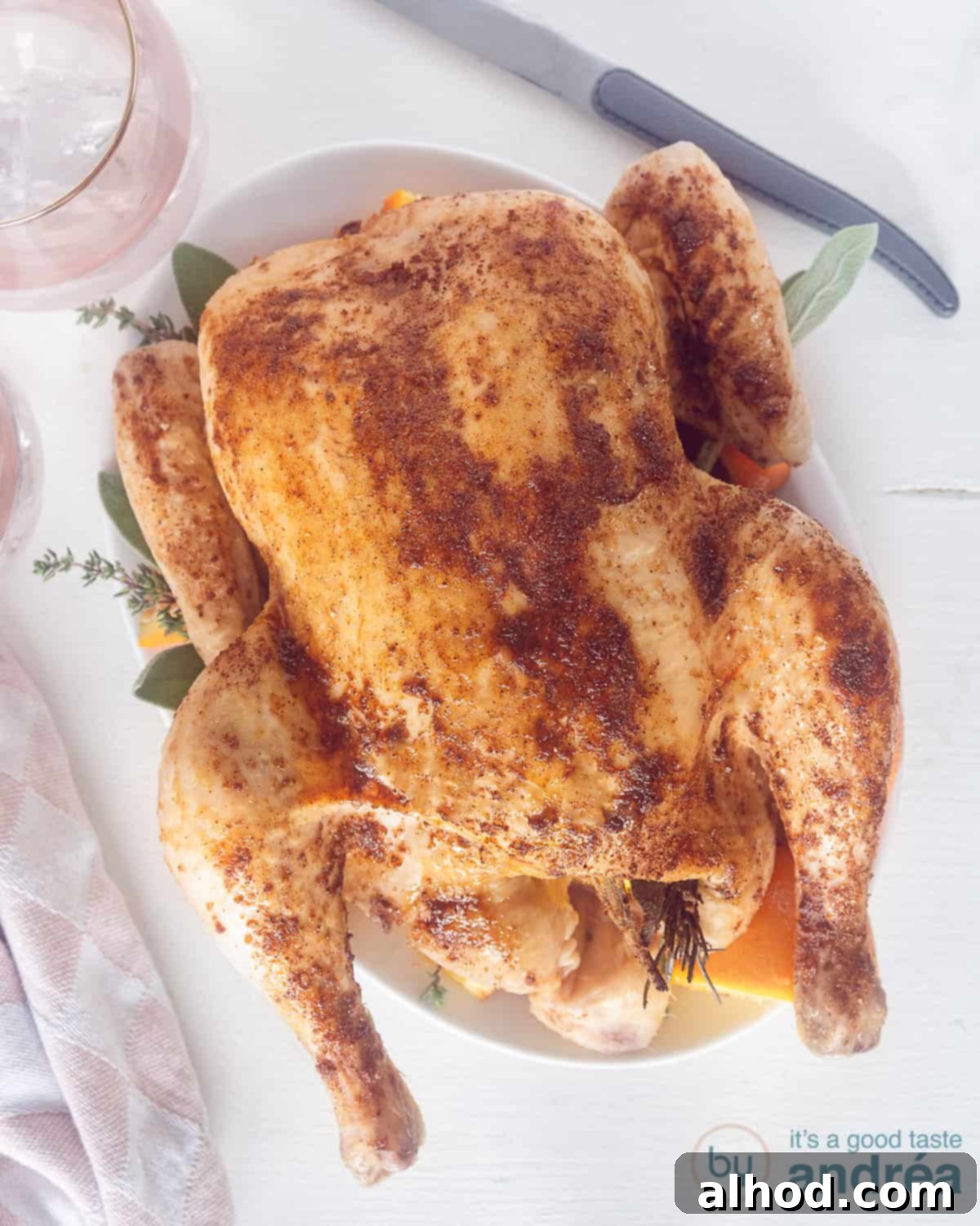 Sticky Orange Honey Roast Chicken 2 Roasted chicken with Honey and Orange from the oven on a white plate. Photographed from above. A knife at the top right, a pink glass at the top left.