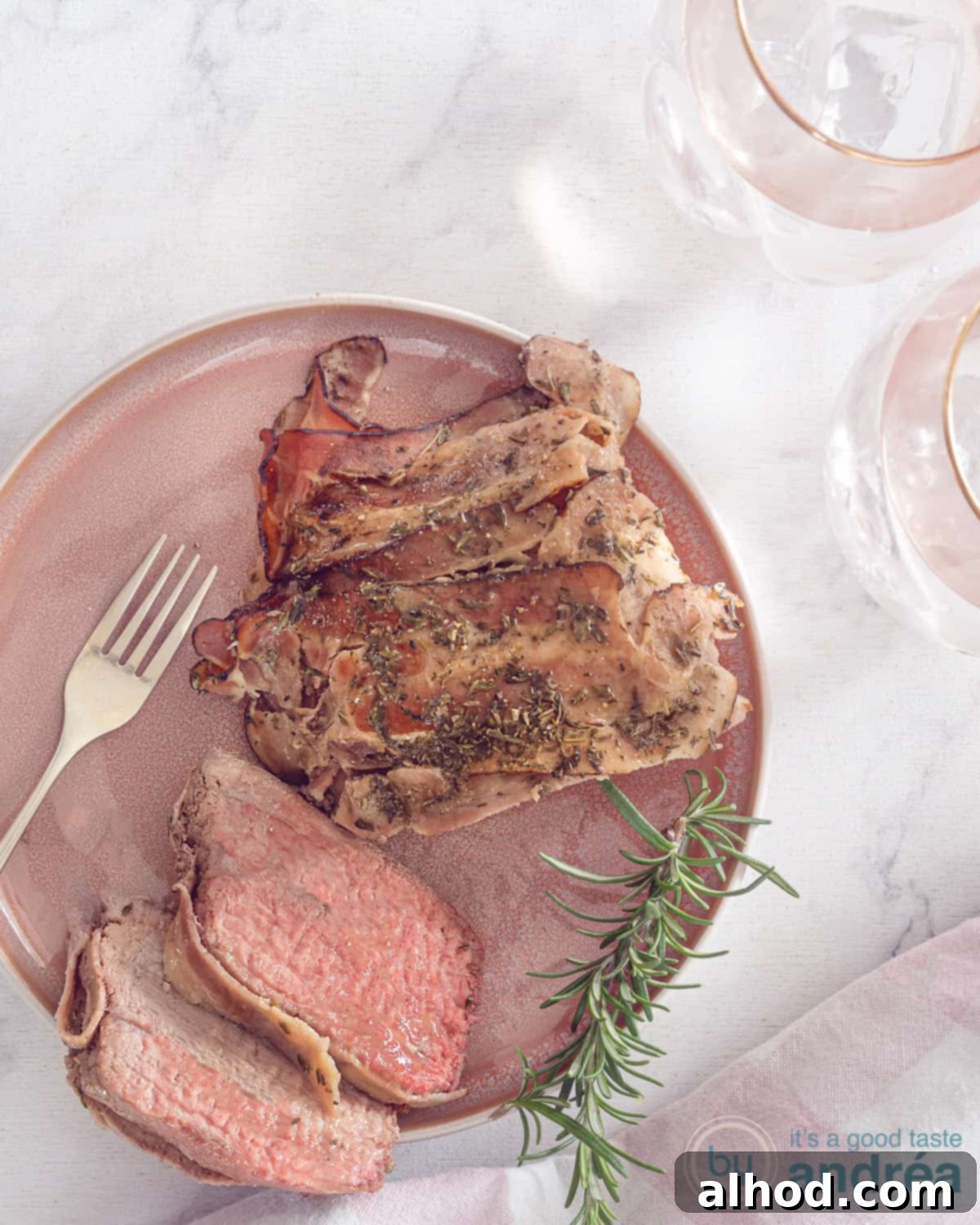 Effortless Bacon-Wrapped Pot Roast 2 A photo from above of a pink plate of roast beef with two slices cut off and wrapped in bacon. A white background.