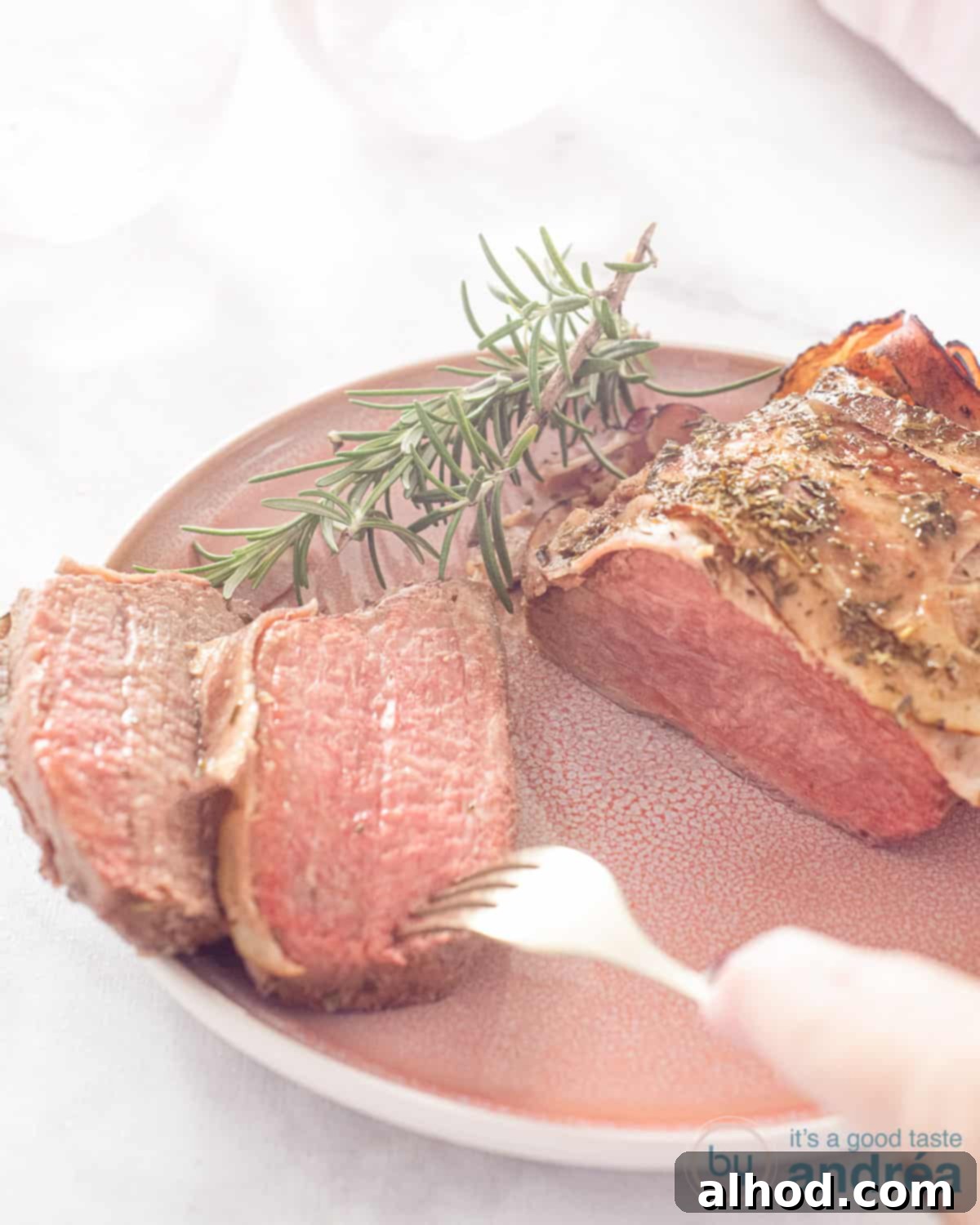 Effortless Bacon-Wrapped Pot Roast 3 An overhead photo of a pink plate with slow cooker roast beef wrapped in bacon. Two slices cut off. A fork is piercing a slice. A white background.