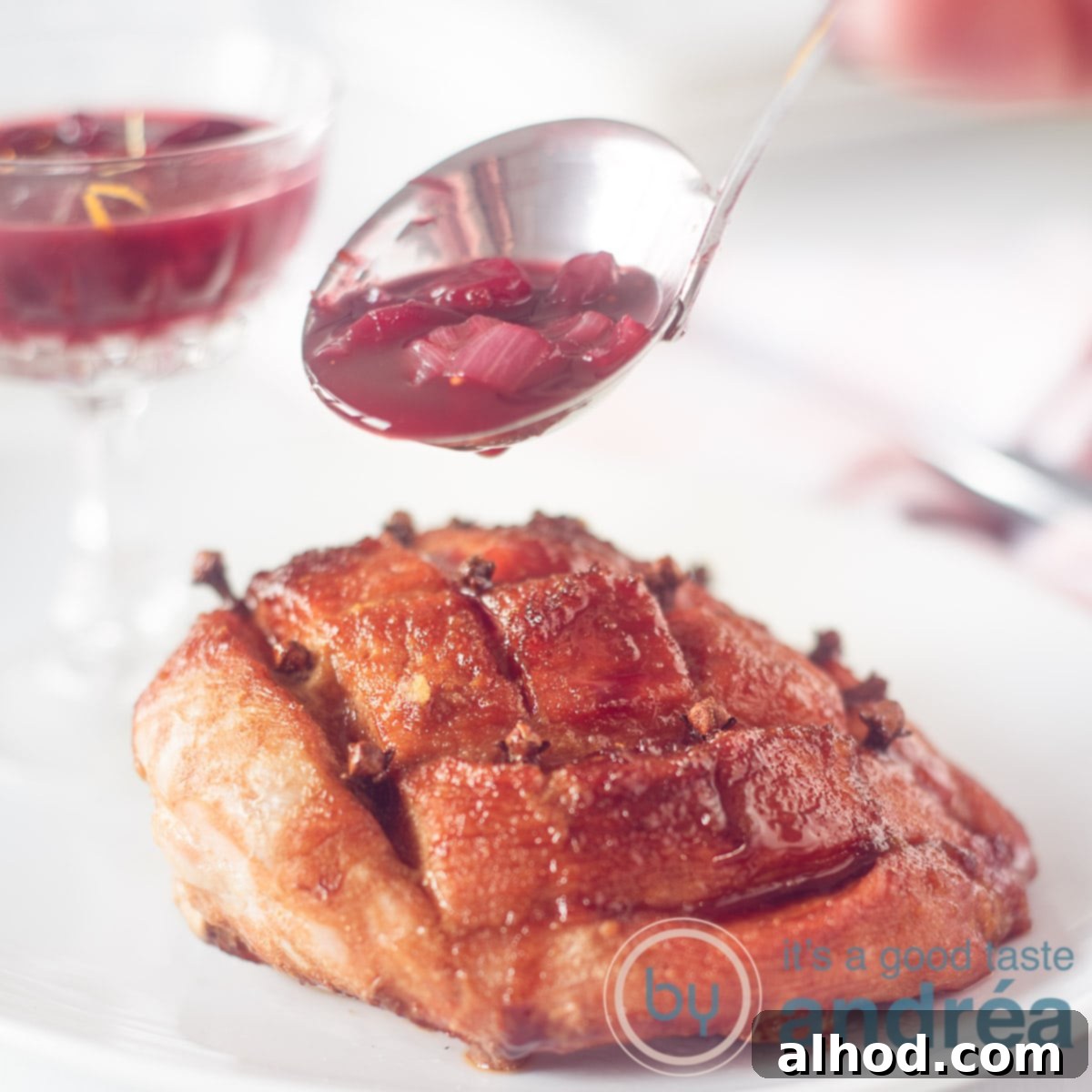 24 Festive Christmas Dinner Recipes 3 A square photo with a white plate of ham on the bone. A sauce ladle filled with cumberland sauce and some sauce in the background. A white background