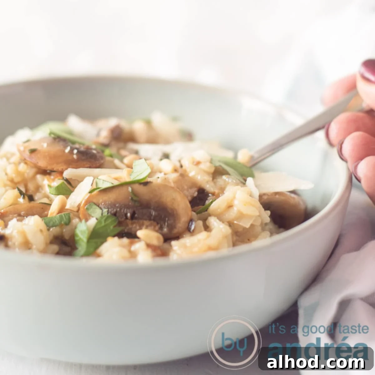 A blue dish with risotto, chestnut mushrooms and herbs. A hand takes a spoon. A white background