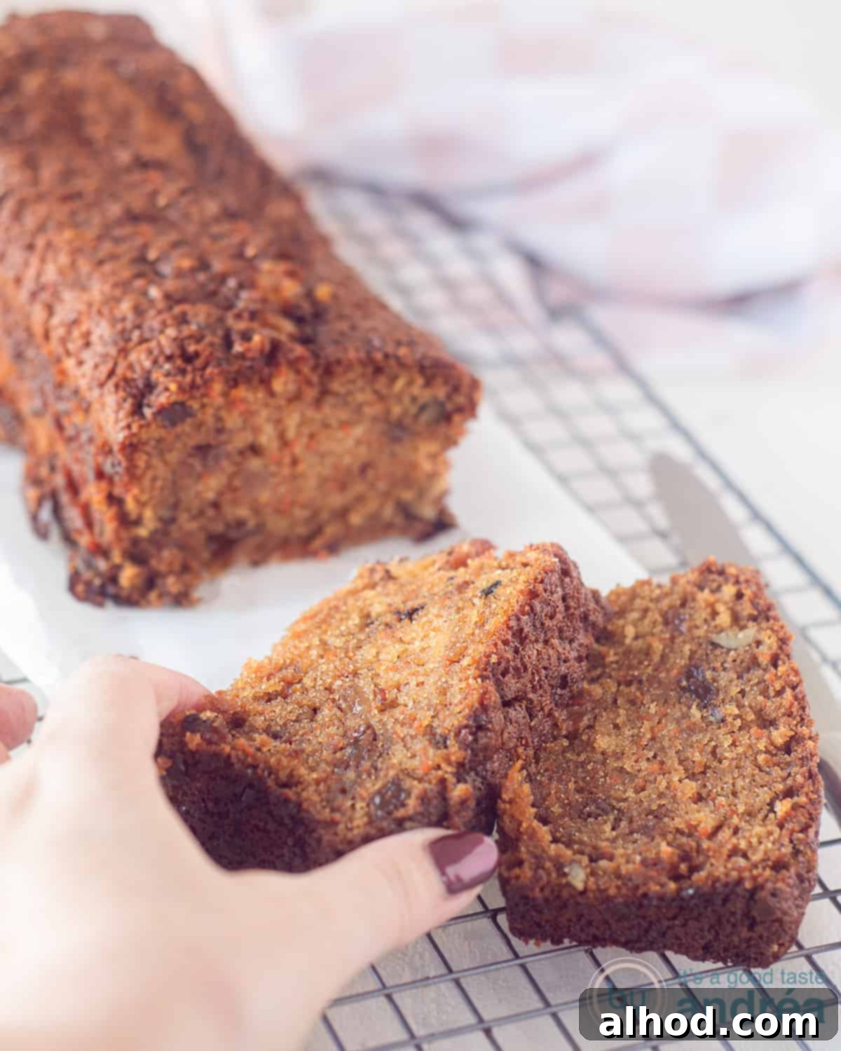 Spiced Carrot Raisin Pound Cake 3 Close-up of a rustic carrot cake, generously studded with walnuts and raisins, cooling on a metal rack. A hand reaches in to take one of the two tempting slices presented on the cutting board.