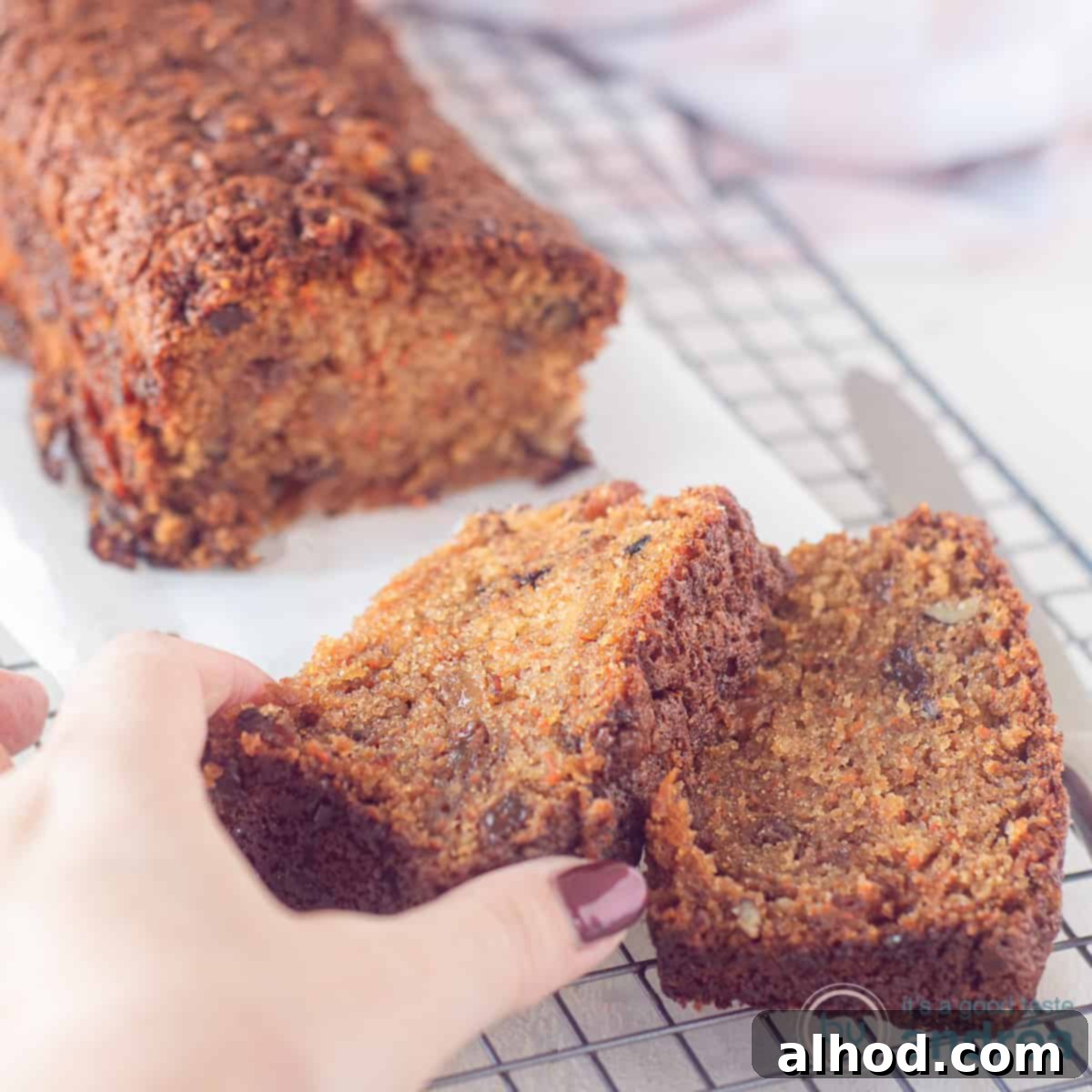 Spiced Carrot Raisin Pound Cake 4 A square photo of a freshly baked carrot, walnut, and raisin pound cake on baking paper on a cooling rack, with two slices already cut and one being taken.
