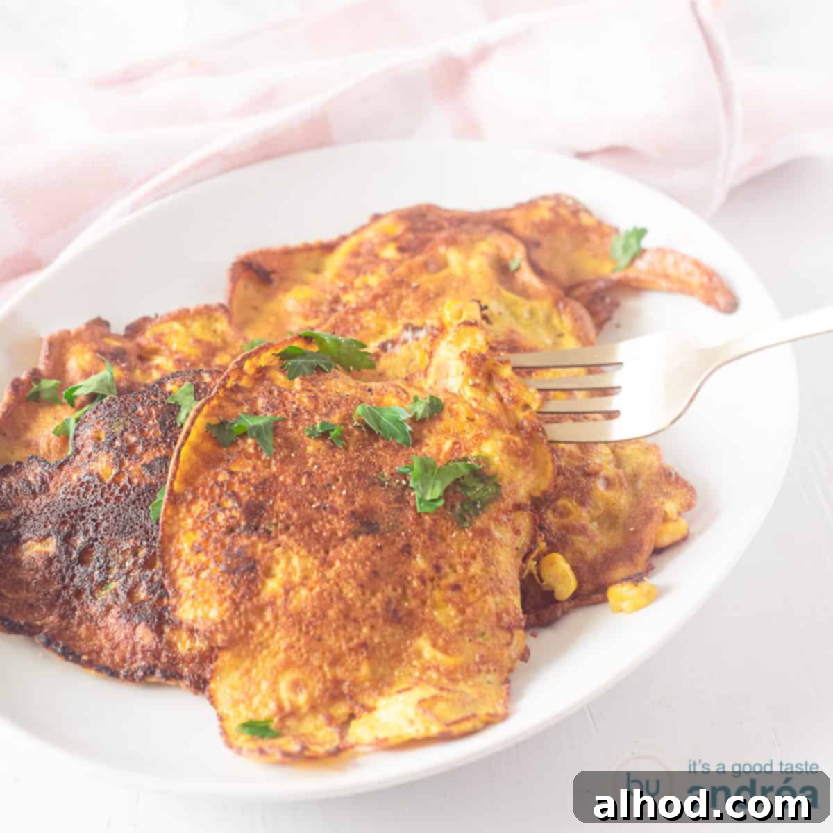Indonesian Corn Fritters 4 A square photo with a white bowl with various corn cookies or Frikadel djagoeng. A pink white tea towel in the background.