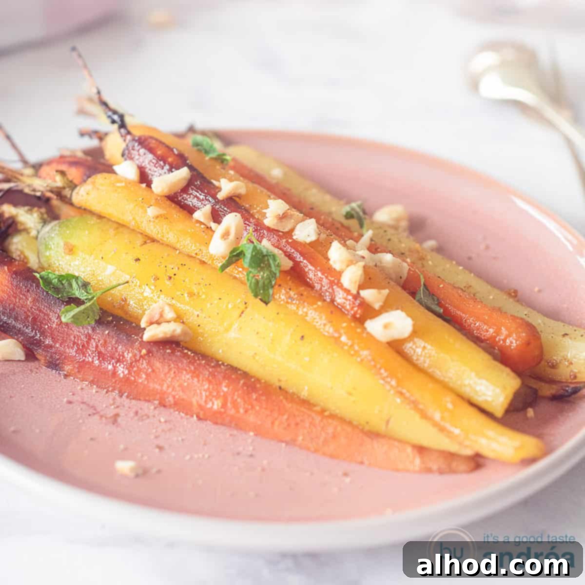 Masala Honey Roasted Carrots 4 A square photo with a pink plate with colored carrots sprinkled with parsley and hazelnuts on a white surface.