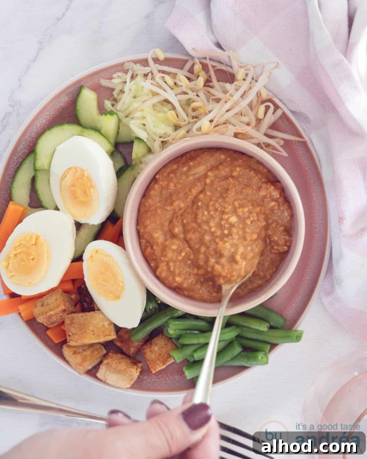 Gado Gado with Creamy Peanut Sauce 3 A vibrant overhead shot of a pink plate showcasing a colorful arrangement of blanched green beans, carrots, crisp cucumber slices, fresh bean sprouts, golden-fried tofu, and halved hard-boiled eggs, all ready to be drizzled with or dipped into a rich satay sauce.