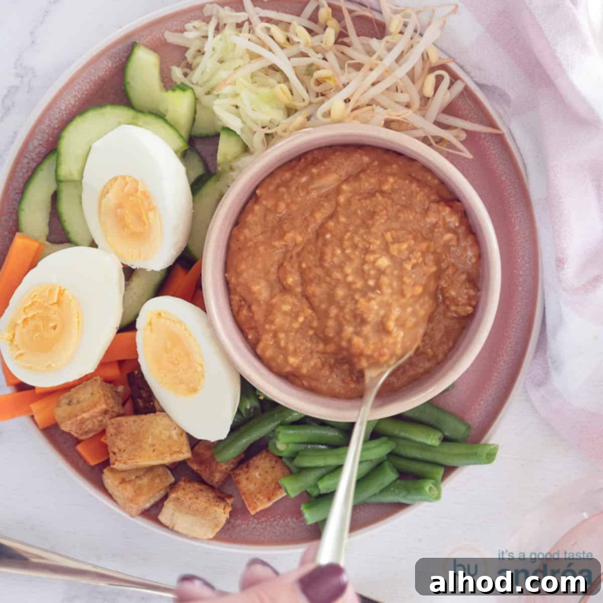 Gado Gado with Creamy Peanut Sauce 4 A square photo featuring a beautiful pink plate filled with perfectly blanched green beans, crisp carrots, fresh bean sprouts, refreshing cucumber slices, golden-fried tofu, and halved hard-boiled eggs, with a small pink bowl of rich peanut satay sauce on the side.