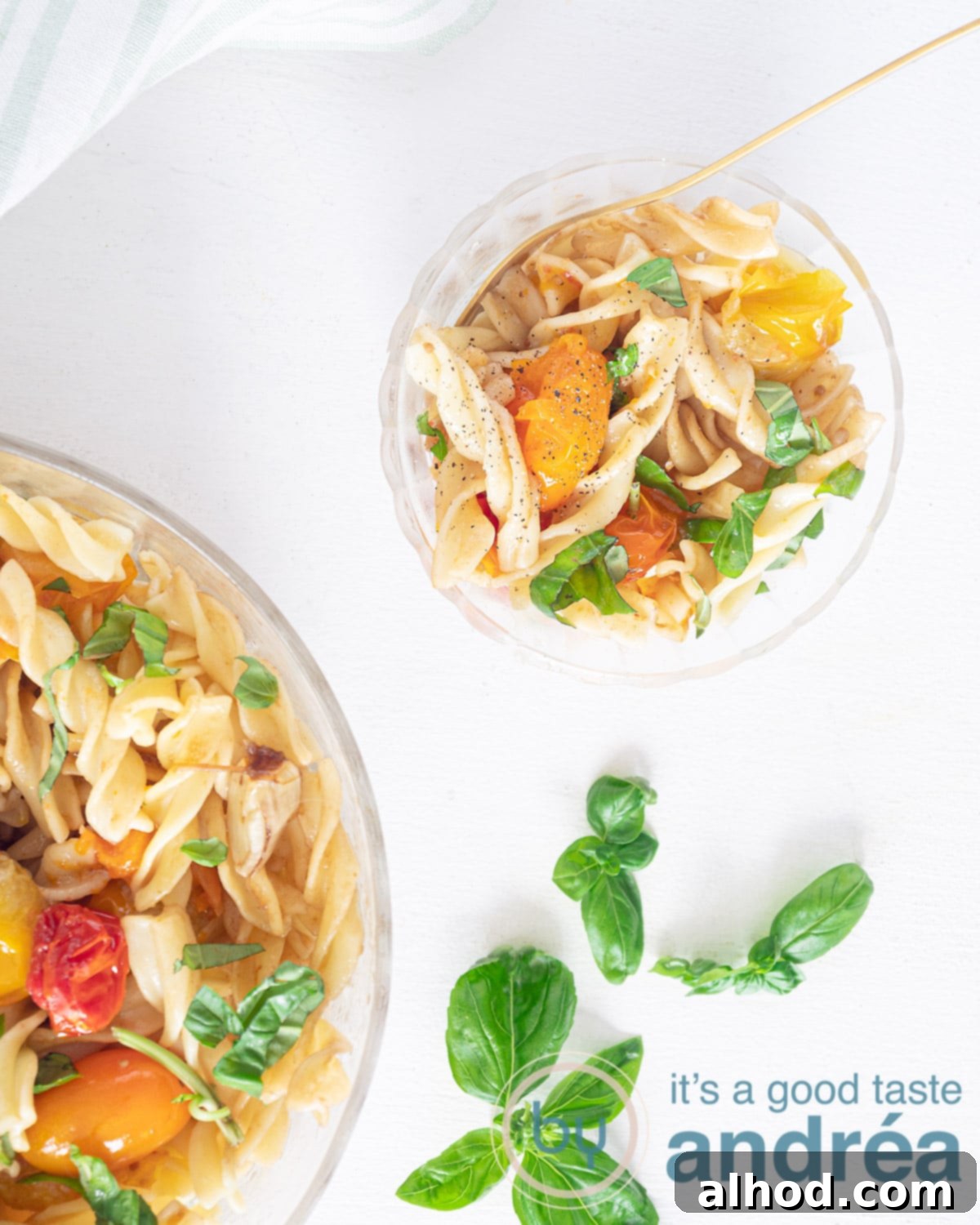 A photo from above of a container of pasta salad at the top right. A second bowl of pasta salad. Basil is placed along the side as a garnish.