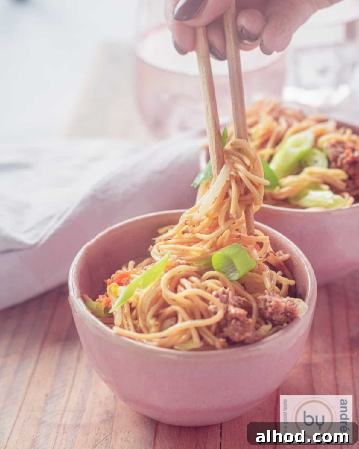 Savory Beef Chow Mein Fresh Vegetables and Signature Sauce 2 An aerial shot of two pink bowls filled with noodles, vegetables and minced meat. Two chopsticks grab a bite of noodles