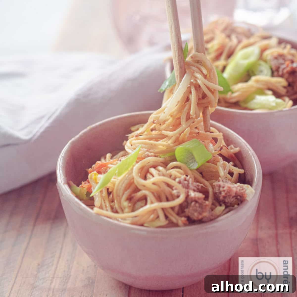 Savory Beef Chow Mein Fresh Vegetables and Signature Sauce 4 A square photo of two pink bowls filled with Chow Mein with ground beef and vegetables. Chopsticks grab noodles
