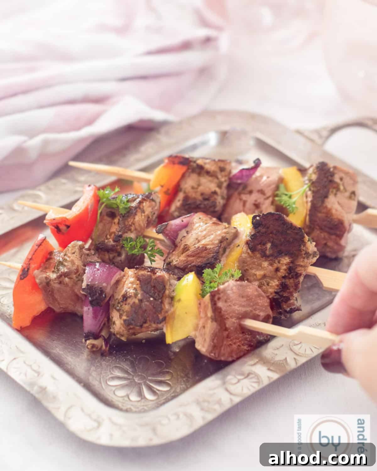 Perfect BBQ Steak & Veggie Skewers 2 An height photo of a silver platter with three skewers of steak, onion and pepper. A hand grabs a stick.