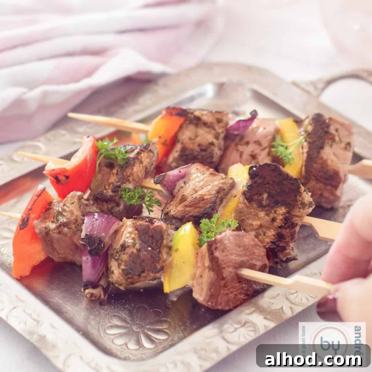 Perfect BBQ Steak & Veggie Skewers 4 A square photo with a silver tray with three steak skewers with onion and pepper, marinated. A hand takes a stick