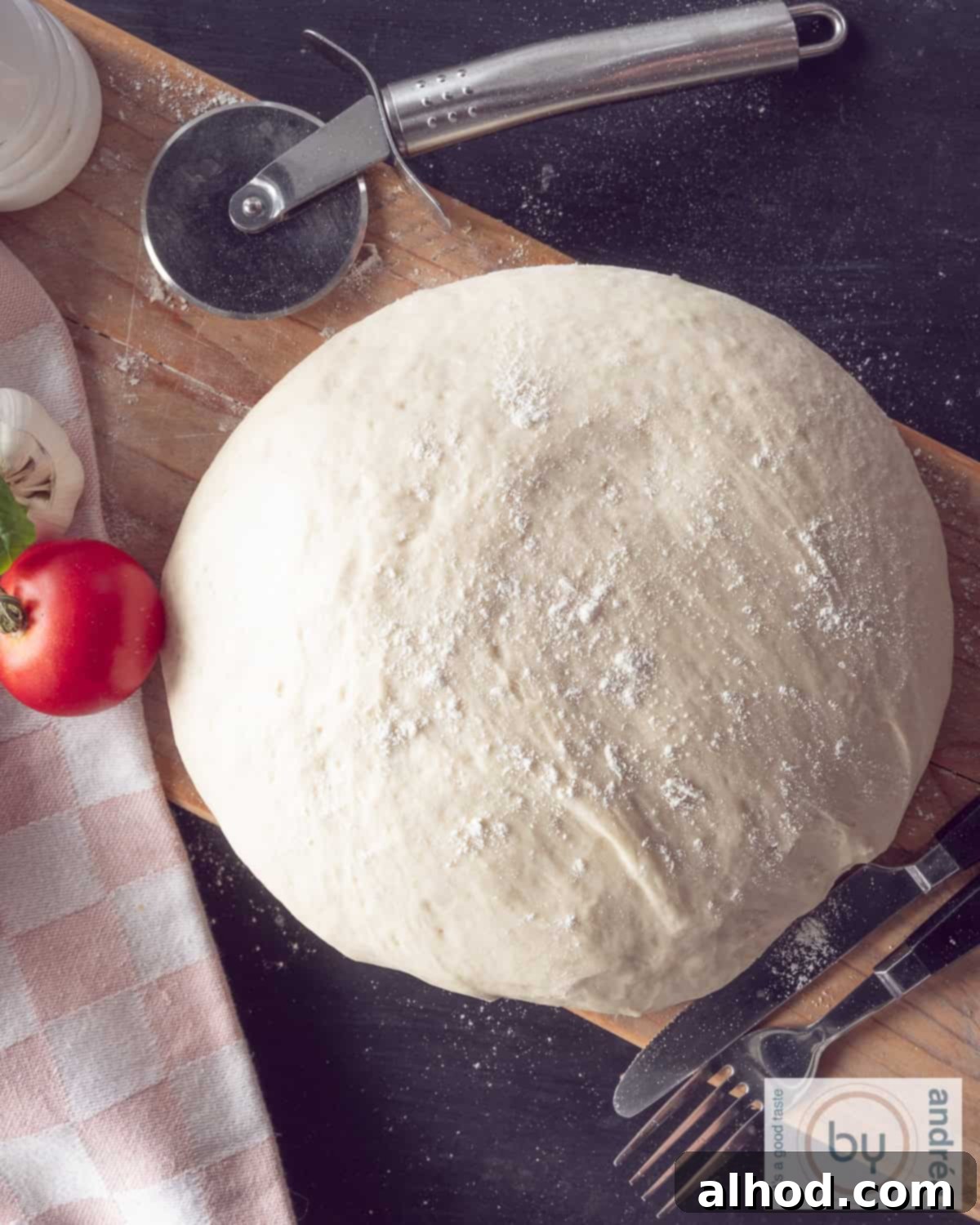 Effortless Homemade Pizza Dough 2 A photo from above of a wooden board on a dark background of a ball of pizza dough, perfectly proofed and ready to be shaped. A pizza cutter is visible at the top, hinting at the delicious outcome.