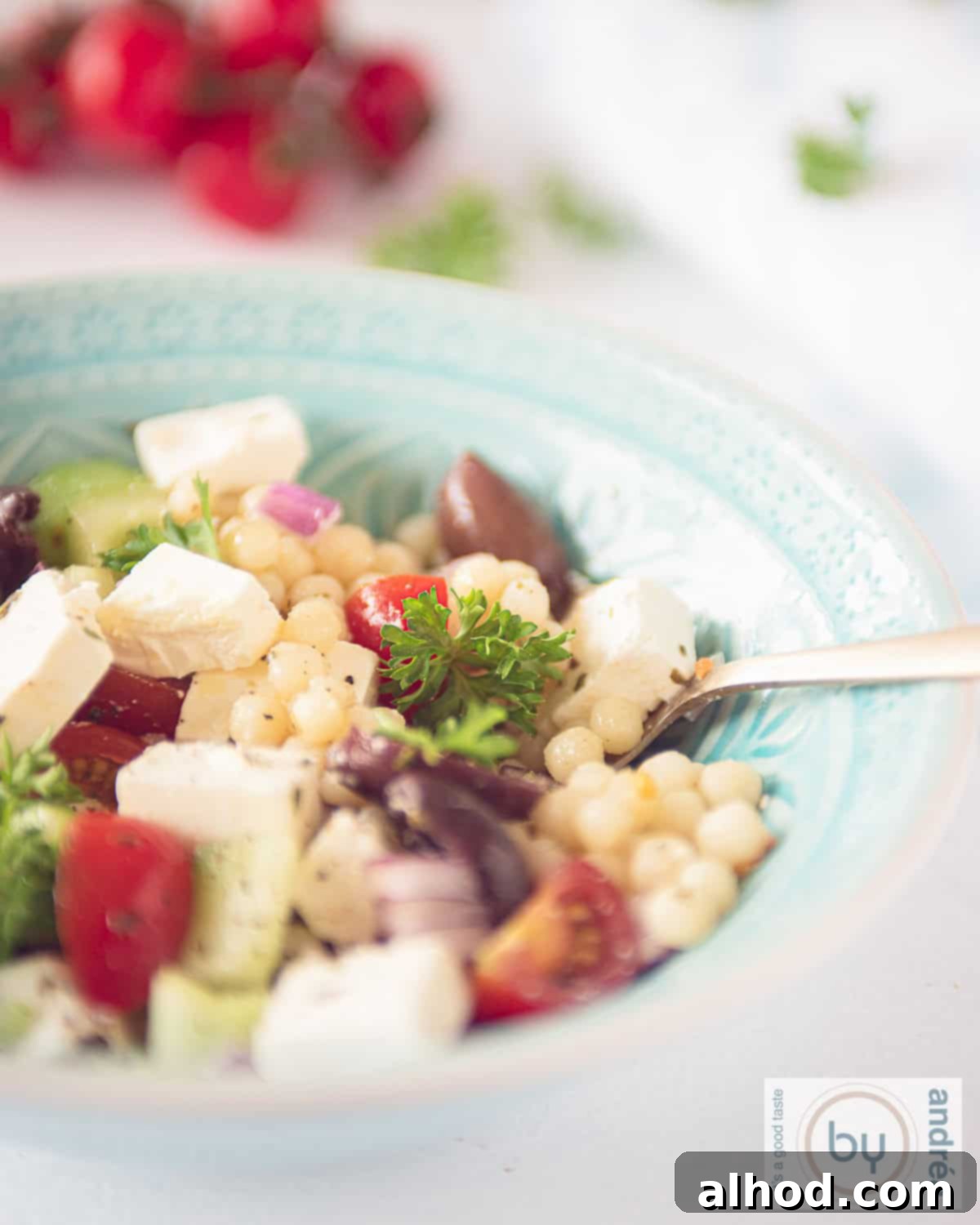 Refreshing Pearl Couscous Salad with Feta, Cucumber, and Bursting Cherry Tomatoes 5 Part of a blue bowl filled with Greek Pearl Couscous salad with feta, cucumber and tomato.