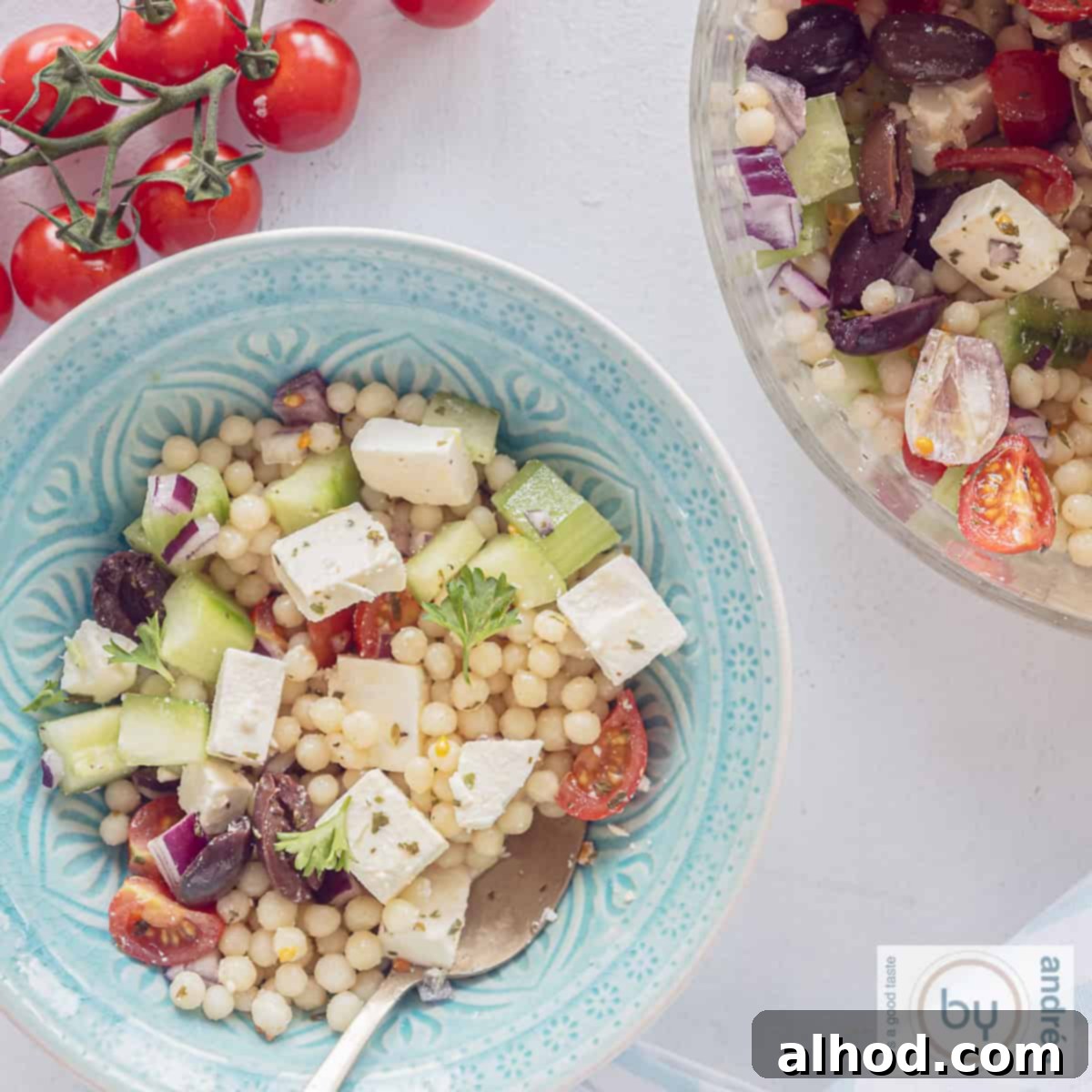Refreshing Pearl Couscous Salad with Feta, Cucumber, and Bursting Cherry Tomatoes 6 A square photo with two bowls, a blue one and part of a glass bowl filled with salad of pearl couscous, cucumber, onion, feta and tomatoes. A bunch of tomatoes above.