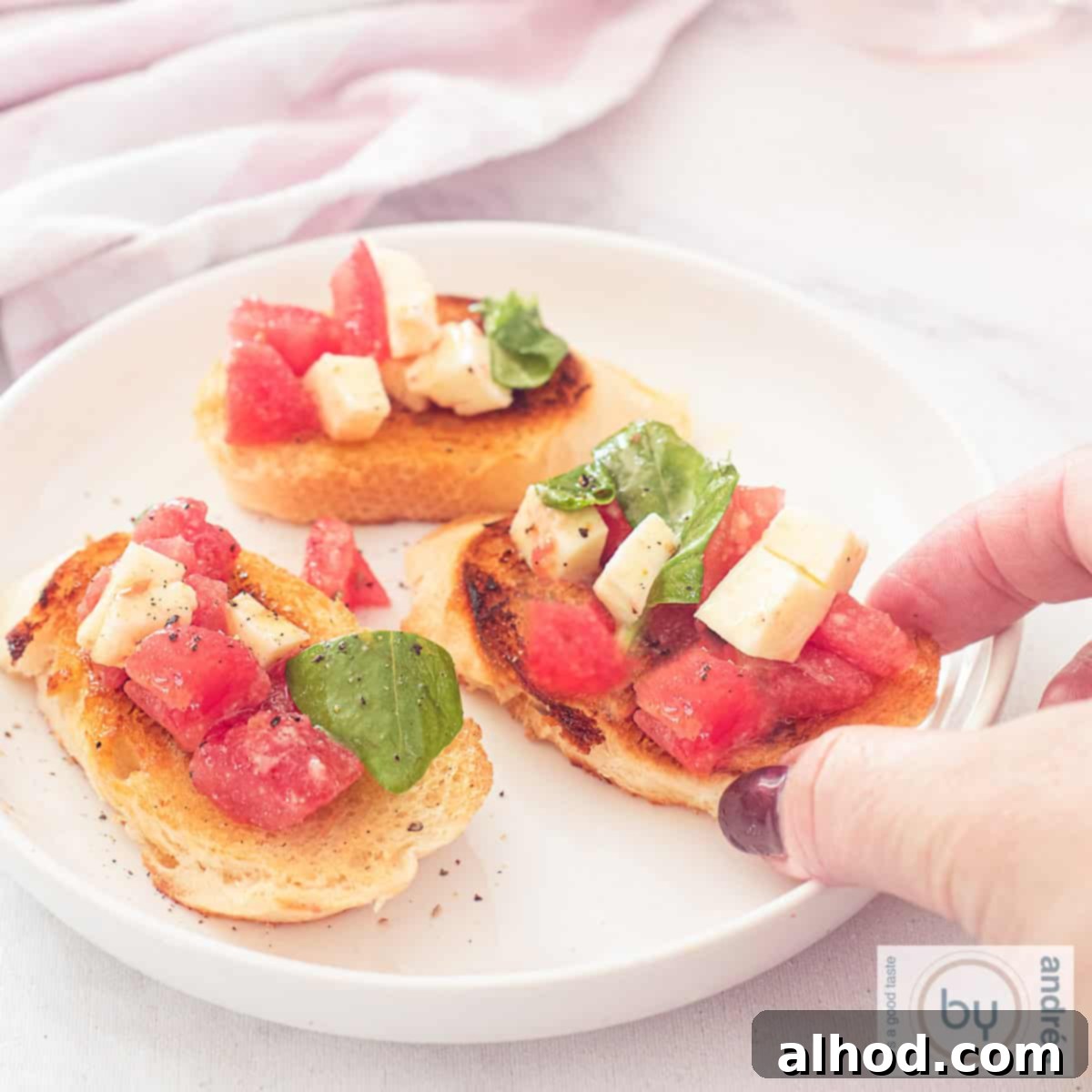 A square photo with a round white plate with three bruschettes with tomato, mozzarella and basil topping