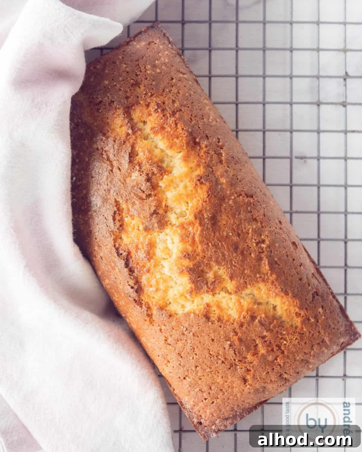 Effortlessly Light and Fluffy Vanilla Applesauce Cake 5 A top-down photo of an applesauce cake on a rack. A pink and white tea towel is placed over part of the cake.