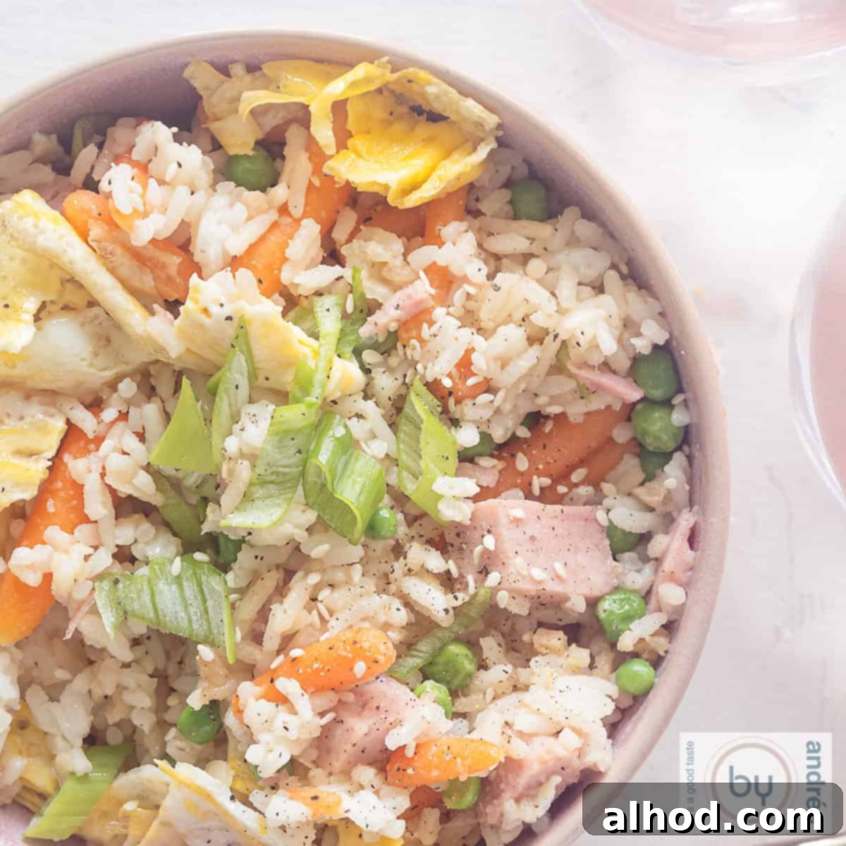 Speedy Ham, Egg, and Vegetable Fried Rice 6 A square photo of a pink bowl with fried rice, vegetables, egg and ham on a white background.