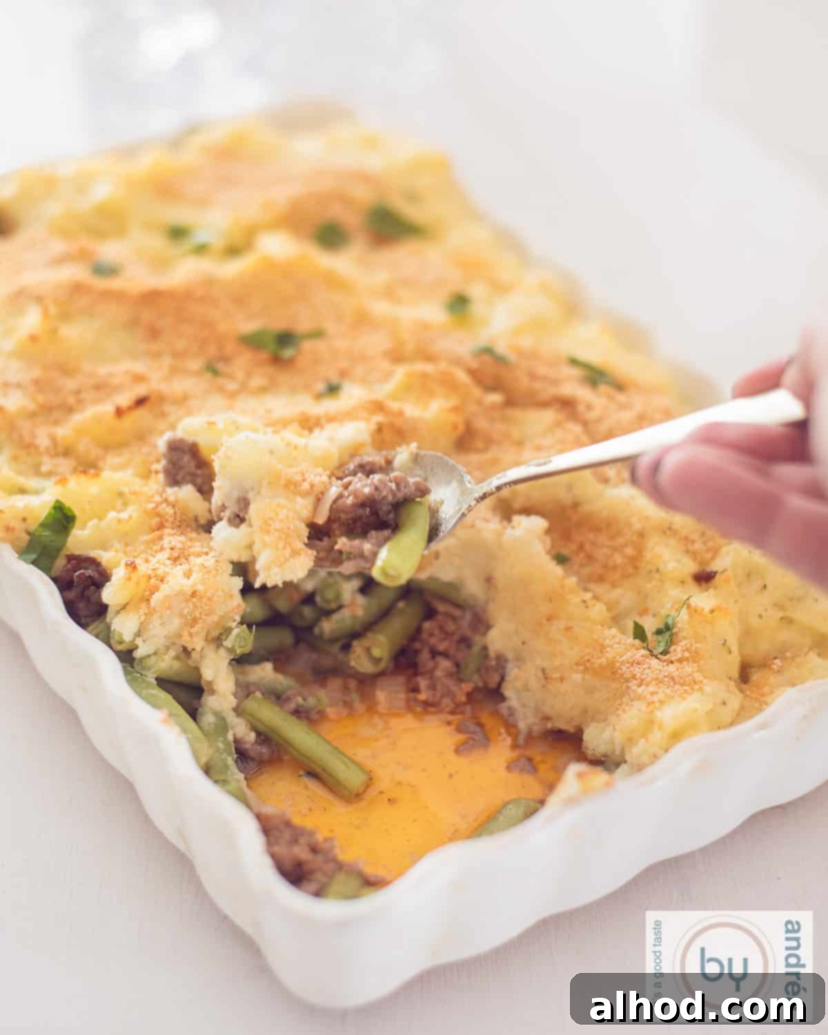 Creamy Boursin Beef and Mashed Potato Casserole 2 A hearty Boursin Mashed Potato and Beef Casserole in a white baking dish, with a spoonful removed, revealing layers of creamy potatoes, seasoned ground beef, and vibrant green beans.