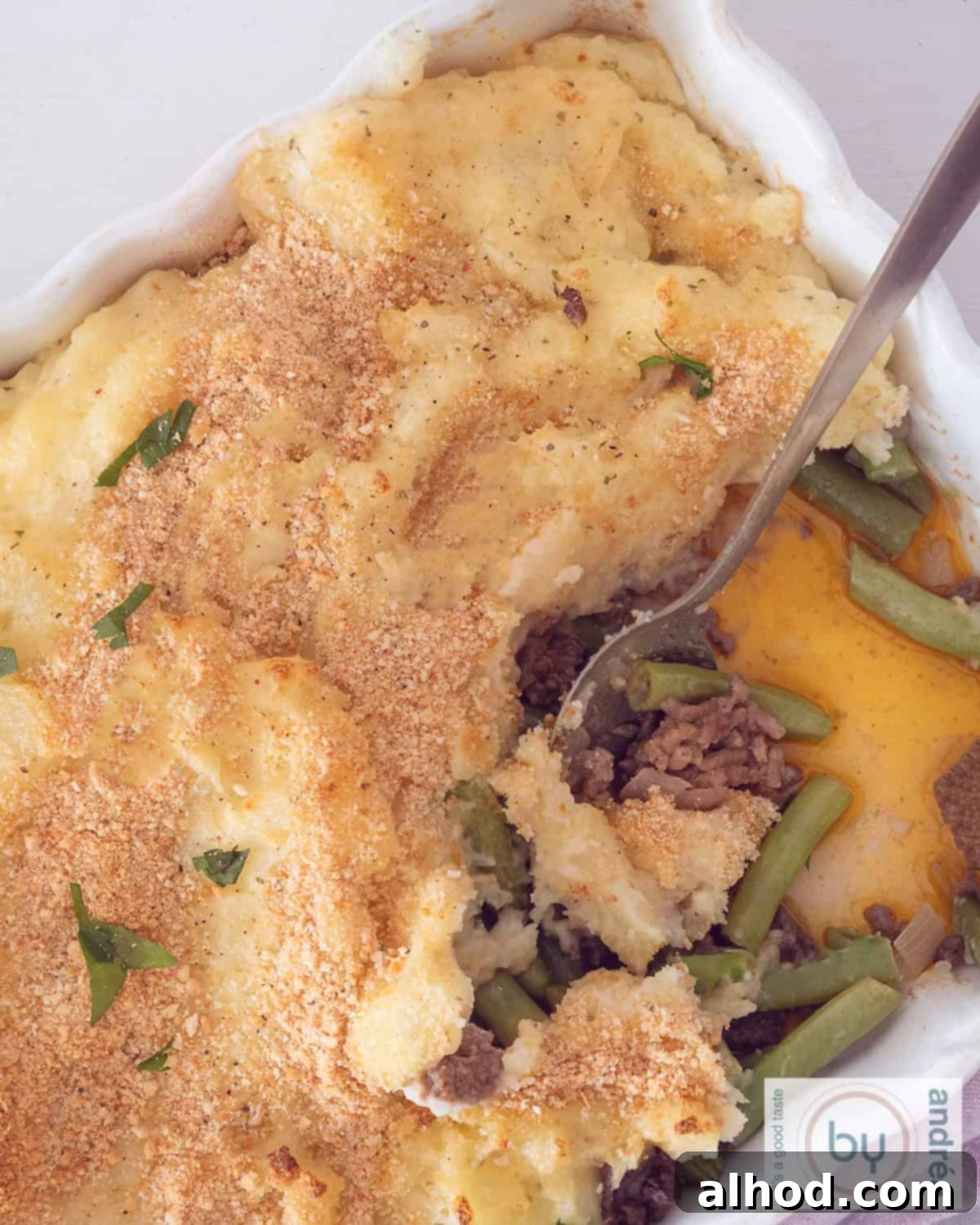Creamy Boursin Beef and Mashed Potato Casserole 5 An overhead view of the baked Boursin Mashed Potato and Beef Casserole in a white dish, with a section scooped out, showing the creamy potato topping, savory beef, and green bean layers.