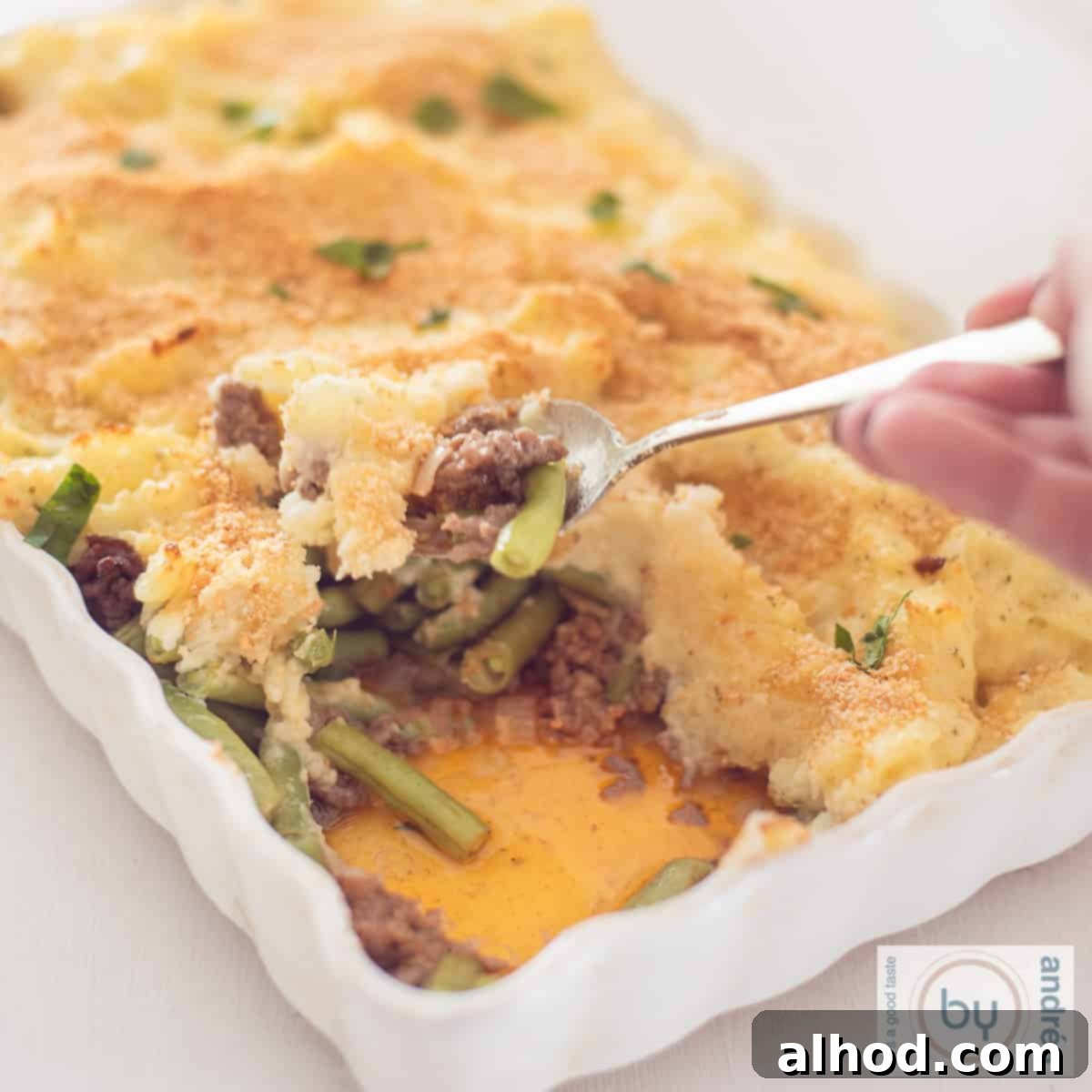 Creamy Boursin Beef and Mashed Potato Casserole 6 A square photo of a white baking dish, with a little bit removed from it, revealing the layers of beans, minced meat and potato puree.