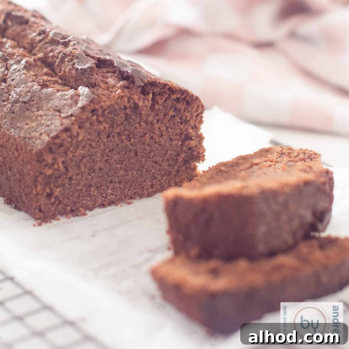 Vanilla-Infused Moist Chocolate Loaf Cake 6 A square photo of a rack with a chocolate cake on it with two slices of cake cut off and lying in front of it.