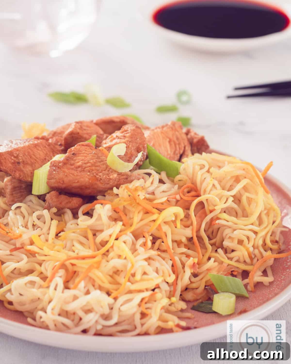 An aerial photo of a pink plate on which noodles with vegetables and Cantonese chicken are scooped. Sprinkled with spring onion.