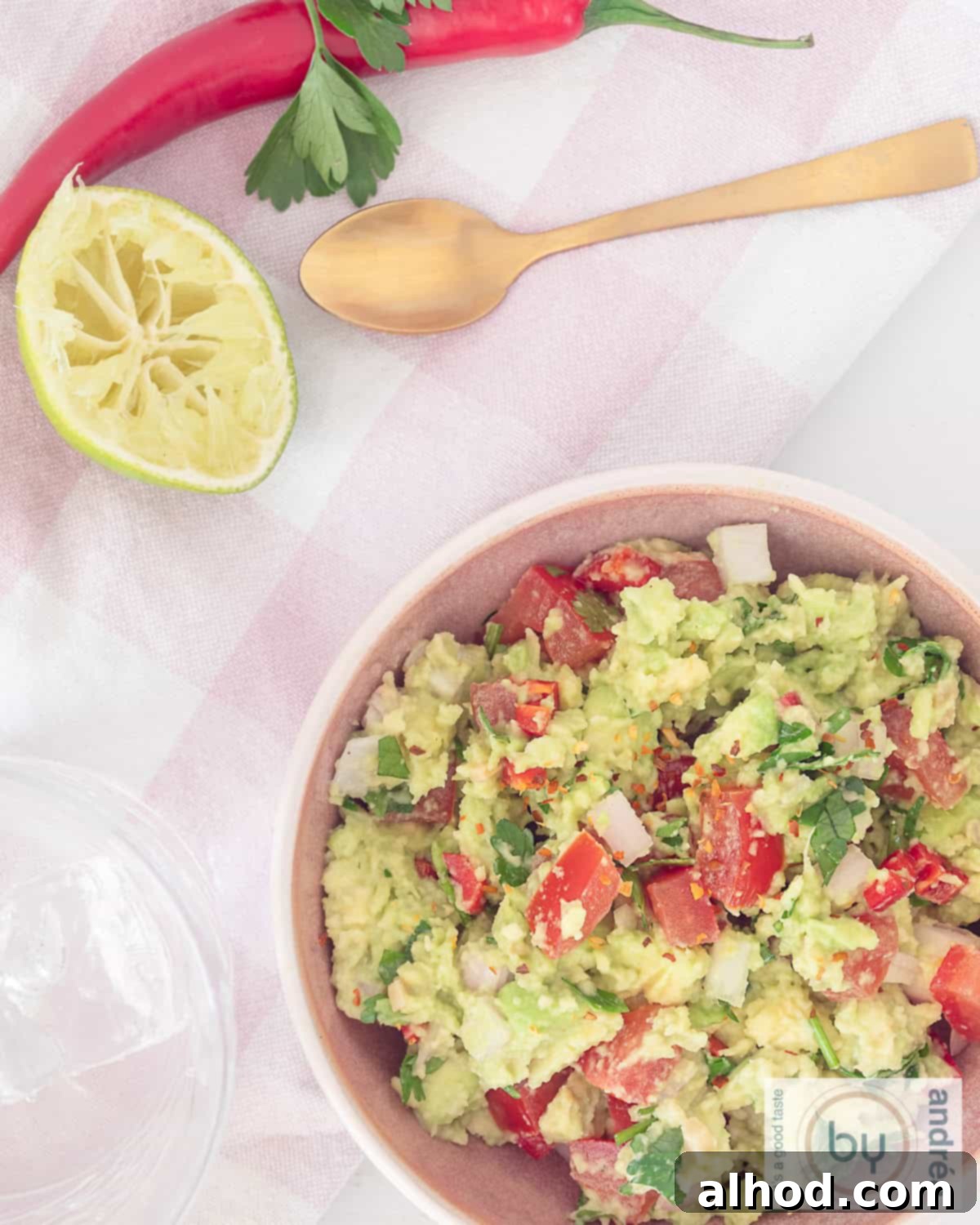 Creamy Avocado & Zesty Lime Guacamole The Perfect Dip 2 A photo from above, bottom right a bowl filled with homemade guacamole garnished with fresh coriander, a squeezed lime wedge, and a golden spoon. Pepper is sprinkled on the side.