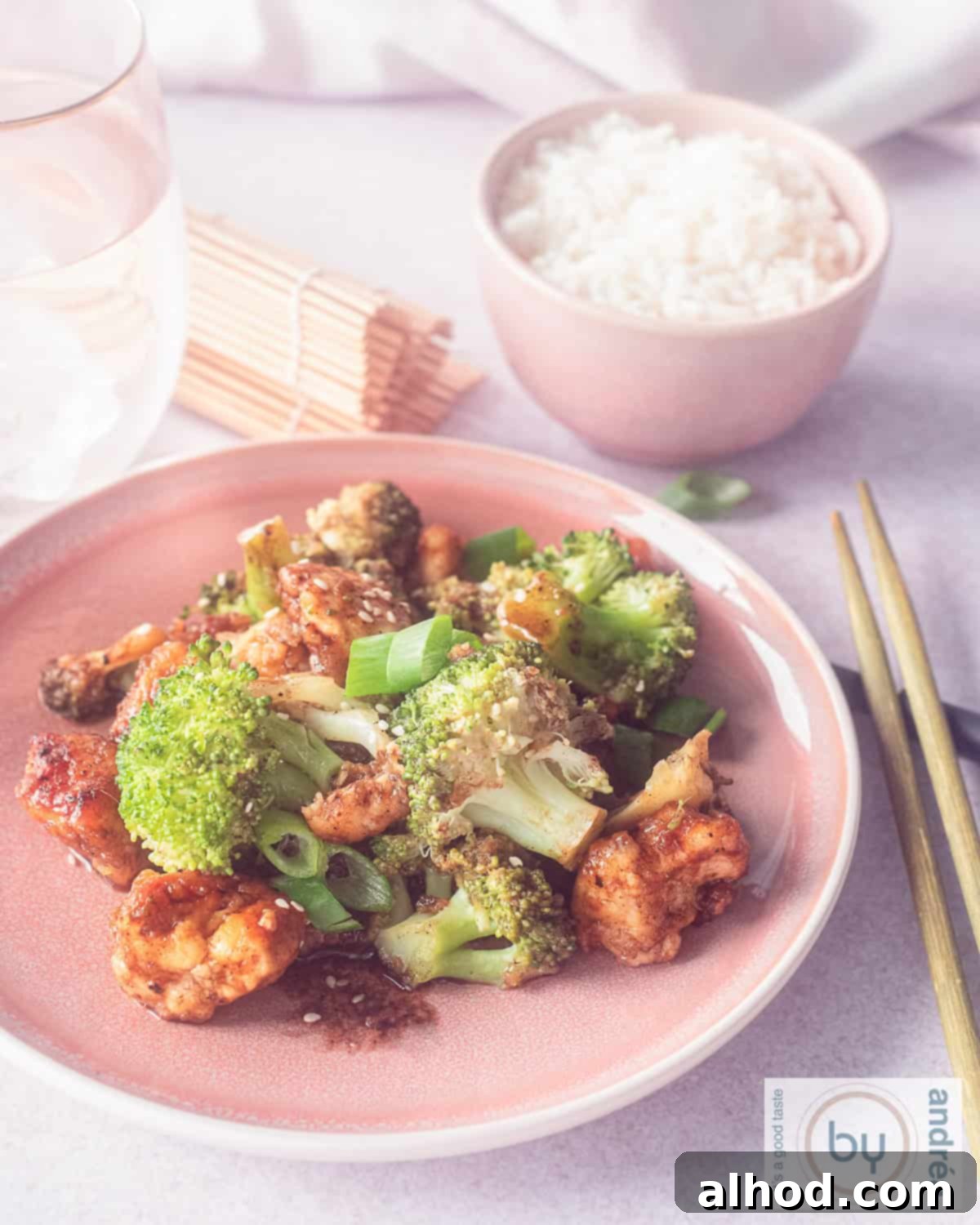 Easy Hoisin Chicken and Broccoli Stir Fry 2 An aerial photo of a pink plate with broccoli, chicken, spring onion in an Asian sauce. In the background a bowl of rice.