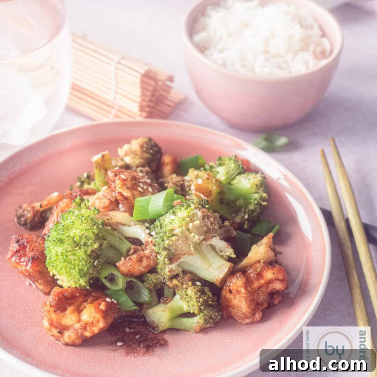 Easy Hoisin Chicken and Broccoli Stir Fry 6 A square photo of a pink plate filled with broccoli, chicken and hoisin sauce. A bowl of rice in the background.