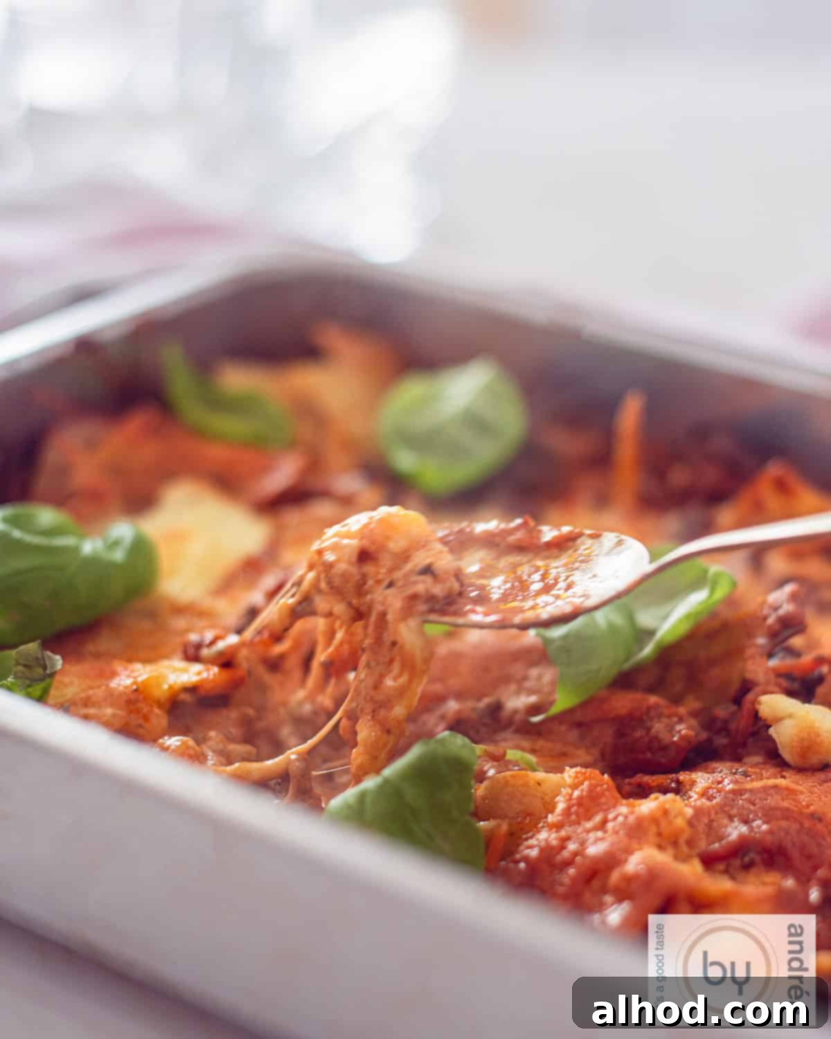 Decadent One Pot Bacon Mascarpone Lasagna 2 An aerial photo of a roasting pan filled with one-pan lasagna with mozzarella, mascarpone, minced meat and tomato sauce. A spoon takes a bite.
