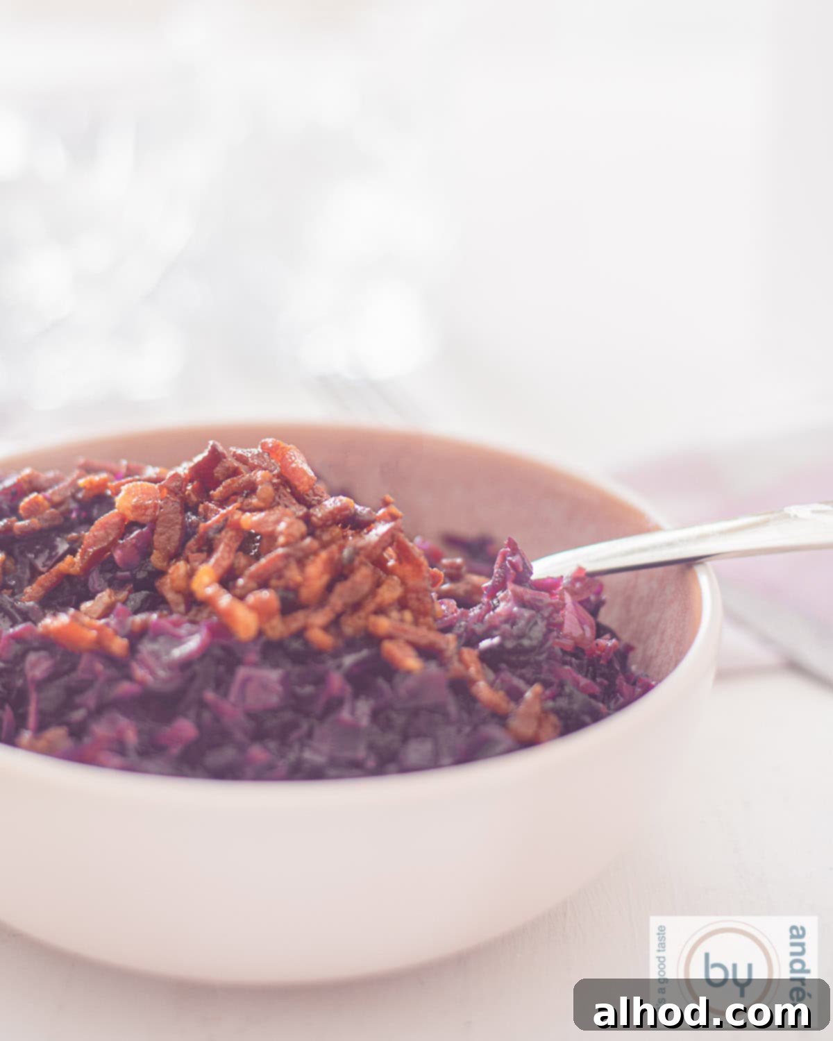 Sweet Sour and Savory German Red Cabbage with Bacon and Apples 2 An aerial photo of a pink bowl of red cabbage filled with fried bacon on top, German red cabbage. A white background.