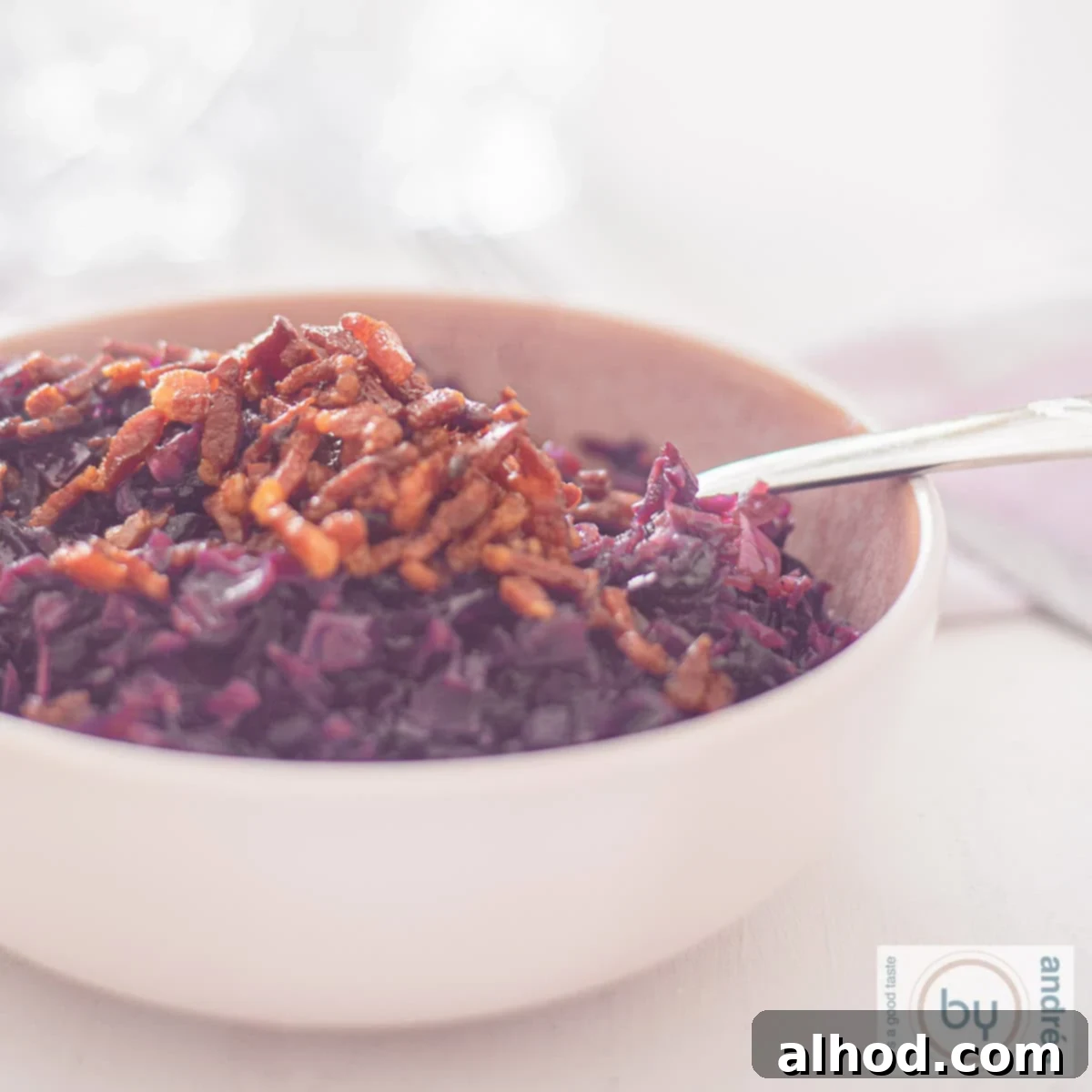 Sweet Sour and Savory German Red Cabbage with Bacon and Apples 6 A square photo of a pink bowl filled with red cabbage and a topping of bacon on a white background.