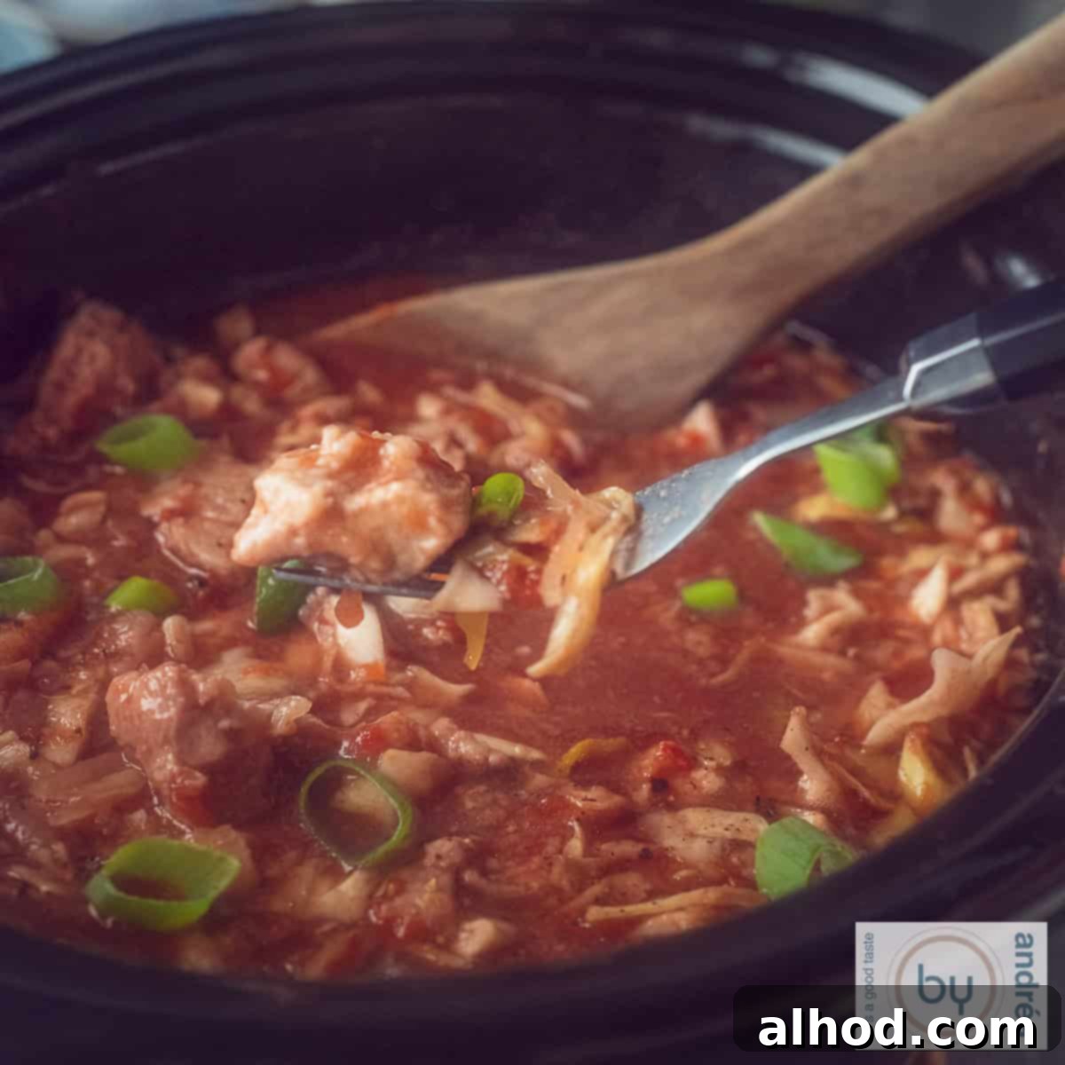 Homestyle Slow Cooker Ham and Cabbage Stew 6 A square photo of part of a slow cooker filled with cabbage, ham steaks and a rich sauce. A fork picks a piece of meat from the pot.