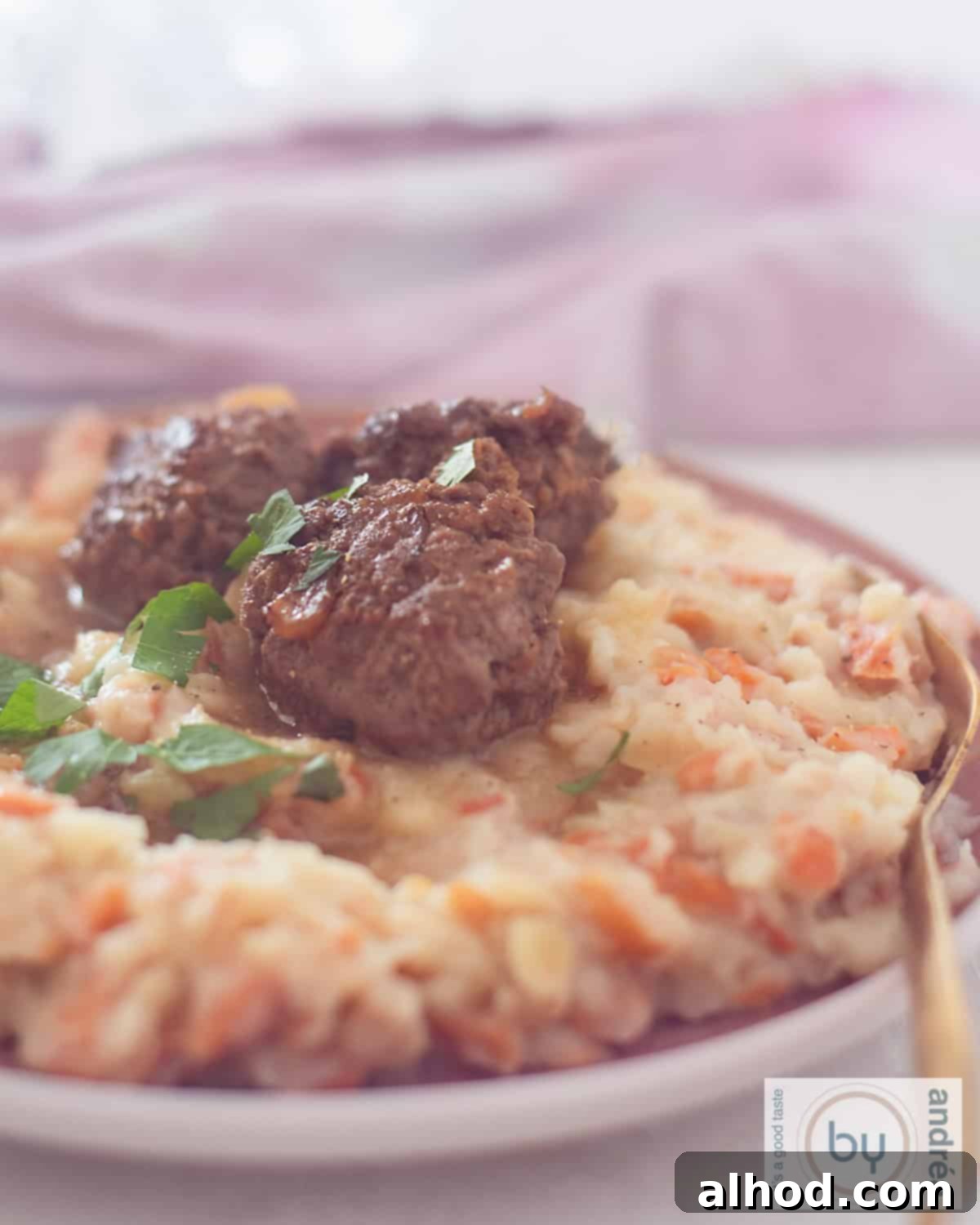 An aerial photo of a pink plate with three spicy meatballs, rich gravy, and creamy wortelstamppot (Dutch carrot mash).