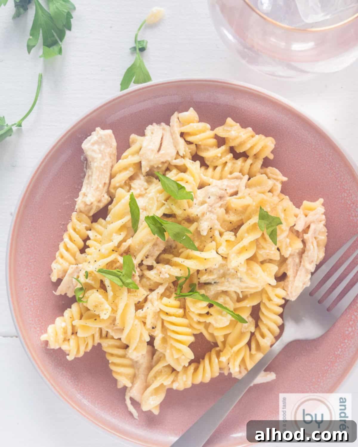 Creamy Garlic Parmesan Chicken and Fusilli in the Slow Cooker 2 A top-down photo of a pink plate with pasta, chicken and creamy parmesan garlic sauce, garnished with fresh parsley.