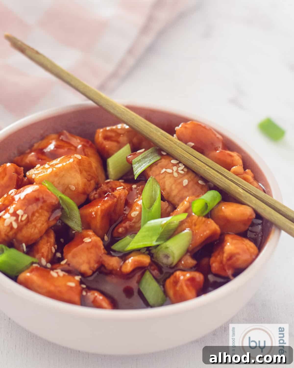 Irresistible Sweet and Sticky Garlic Chicken 2 An aerial shot of a pink bowl of sticky chicken, spring onion and sesame seeds. Two golden chopsticks are placed on top.