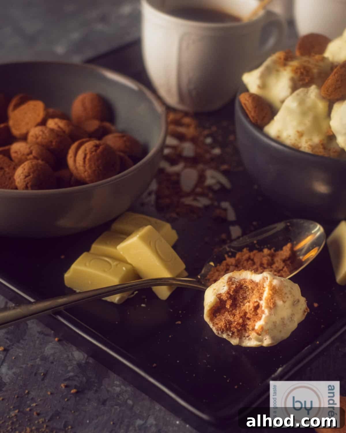Decadent White Chocolate Pepernoten Truffles 5 An height photo with a white chocolate truffle where the inside of cream cheese with pepernoten can be seen on a dark background. In the background, white chocolate, gingerbread and more truffles.