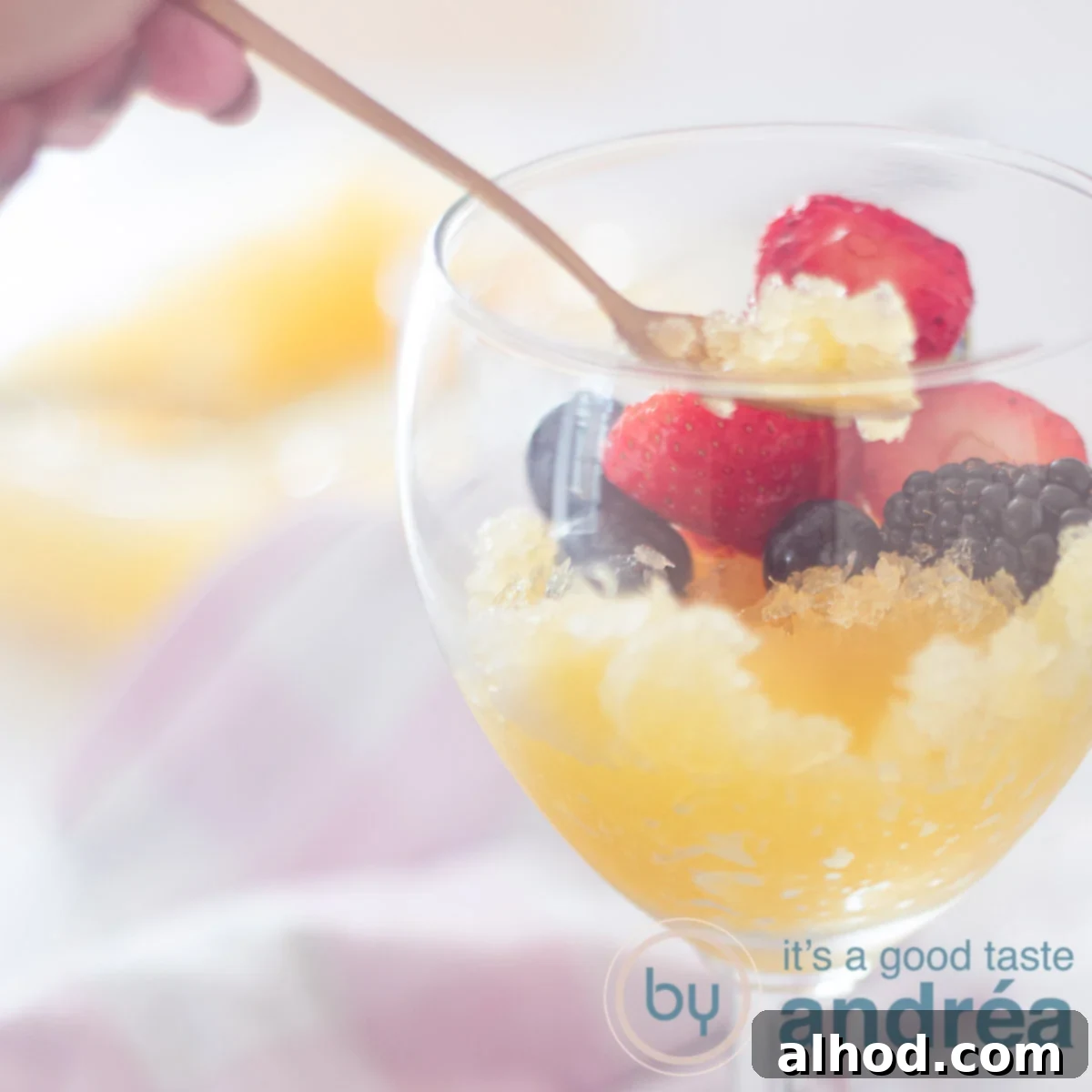 a square photo with part of a glass filled with orange beer sorbet and topped with fresh fruit. A golden spoon